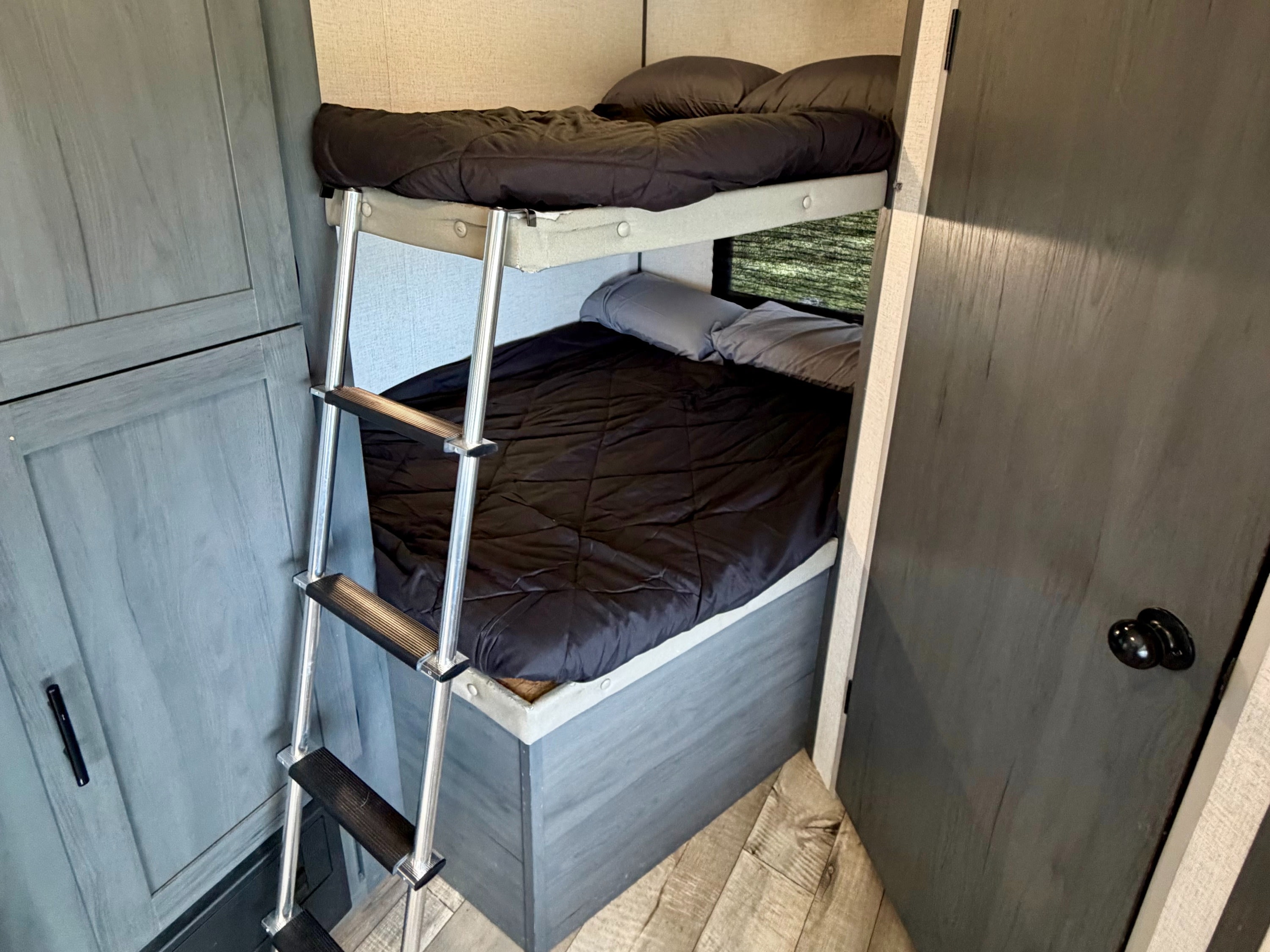 RV rental bunk beds featuring a ladder & dark bedding. A compact, cozy sleeping area inside this camper for travelers.. Dutchmen Aspen Trail LE 26BH 2022
