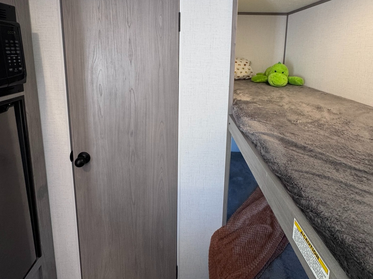 Inside an RV rental: a cozy bunk bed with a green dinosaur, next to a wood-grain door. Compact and ready for adventure.. Dutchmen Coleman Lantern LT 2022