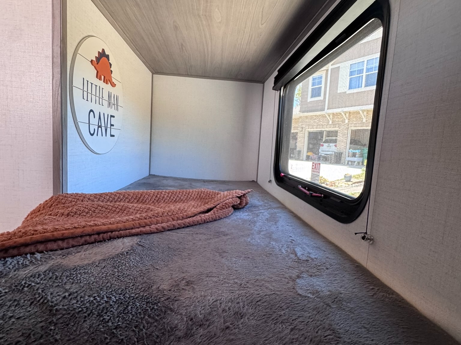 Cozy RV rental bunk bed with a fluffy blanket, "Little Man Cave" dinosaur sign, and a view from the window.. Dutchmen Coleman Lantern LT 2022