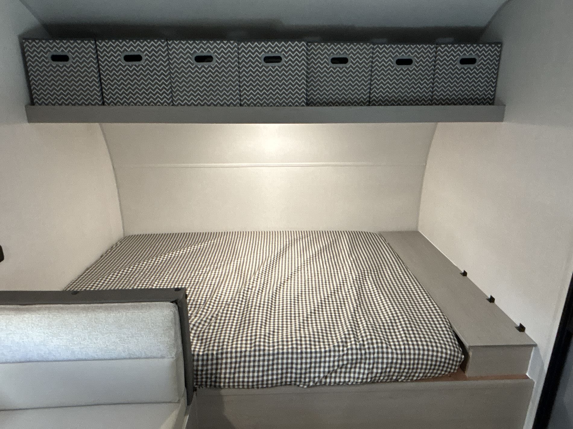 Compact rv rental bedroom featuring a checkered bed, overhead shelf with chevron storage bins, and a side platform.. Coachmen Clipper 17BH 2026