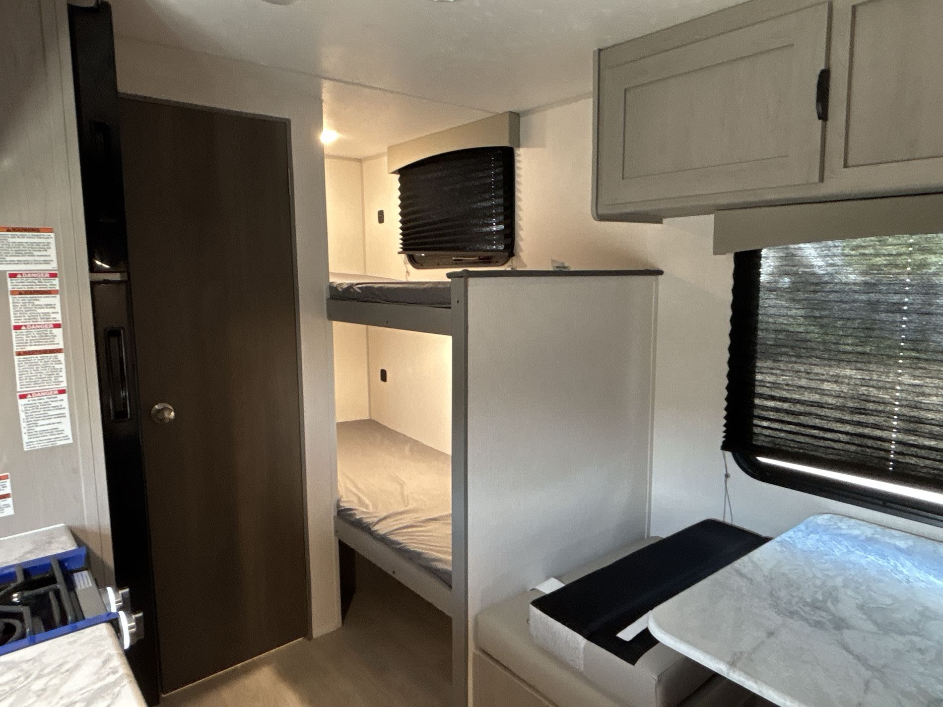 This RV rental interior features comfy bunk beds, a dinette, and a compact kitchen area with stove & fridge, plus overhead cabinets.. Coachmen Clipper 17BH 2026