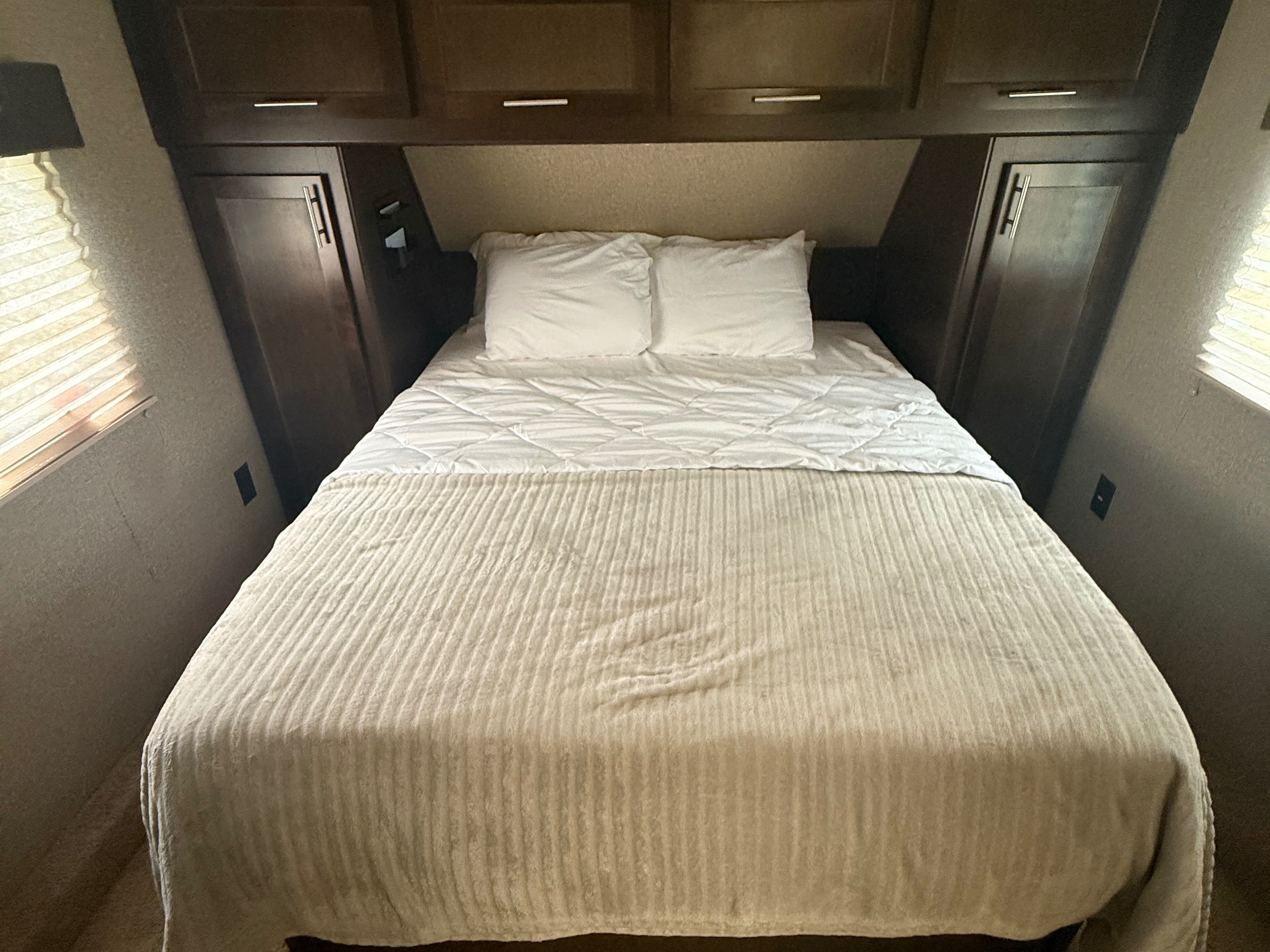 Cozy RV rental bedroom with a neatly made bed, white pillows, overhead cabinets, and side storage.. Forest River Wolf Pack 2019