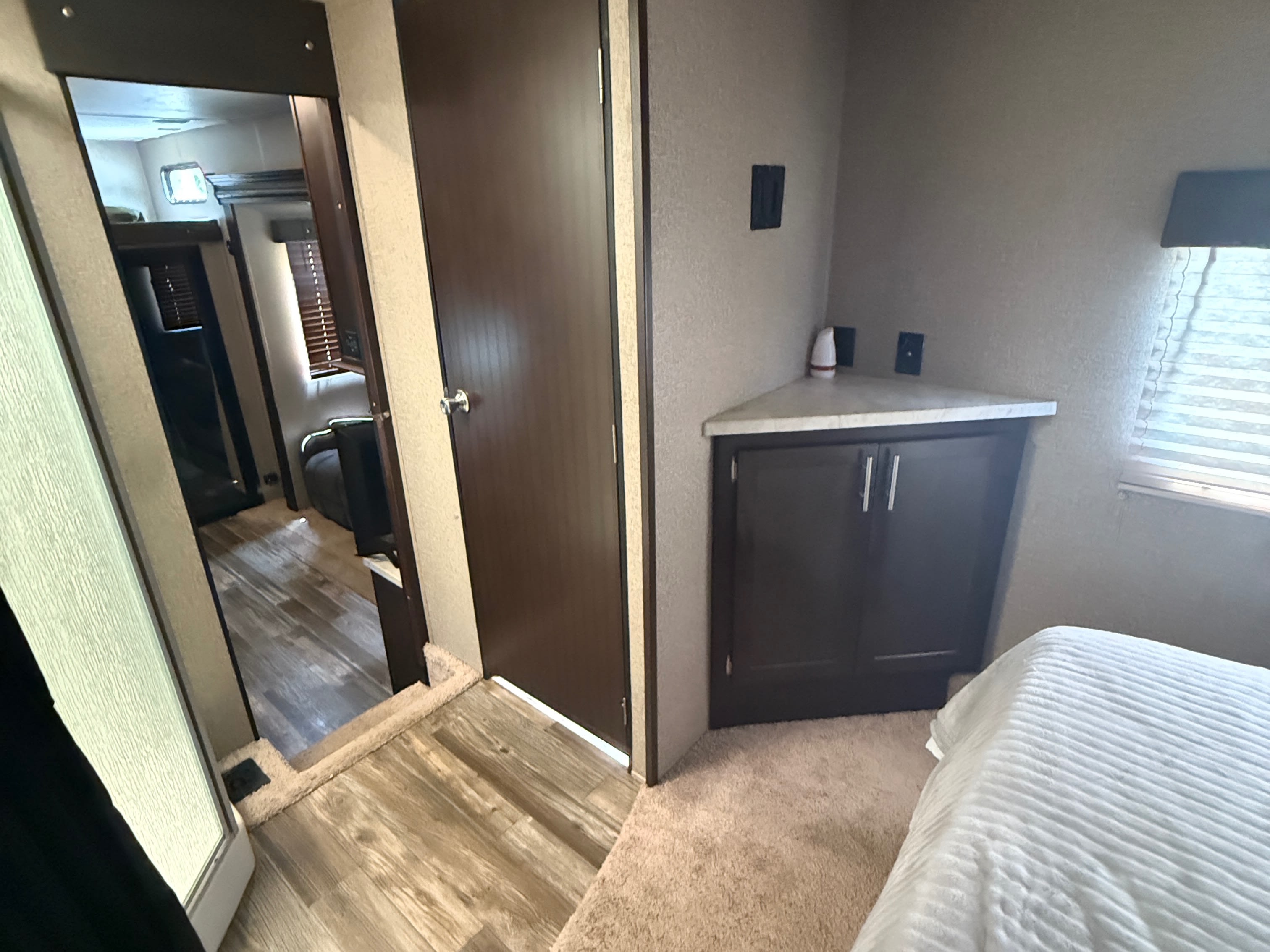 This cozy RV rental bedroom features a comfortable bed, corner storage, and a mirror reflecting the main living area.. Forest River Wolf Pack 2019