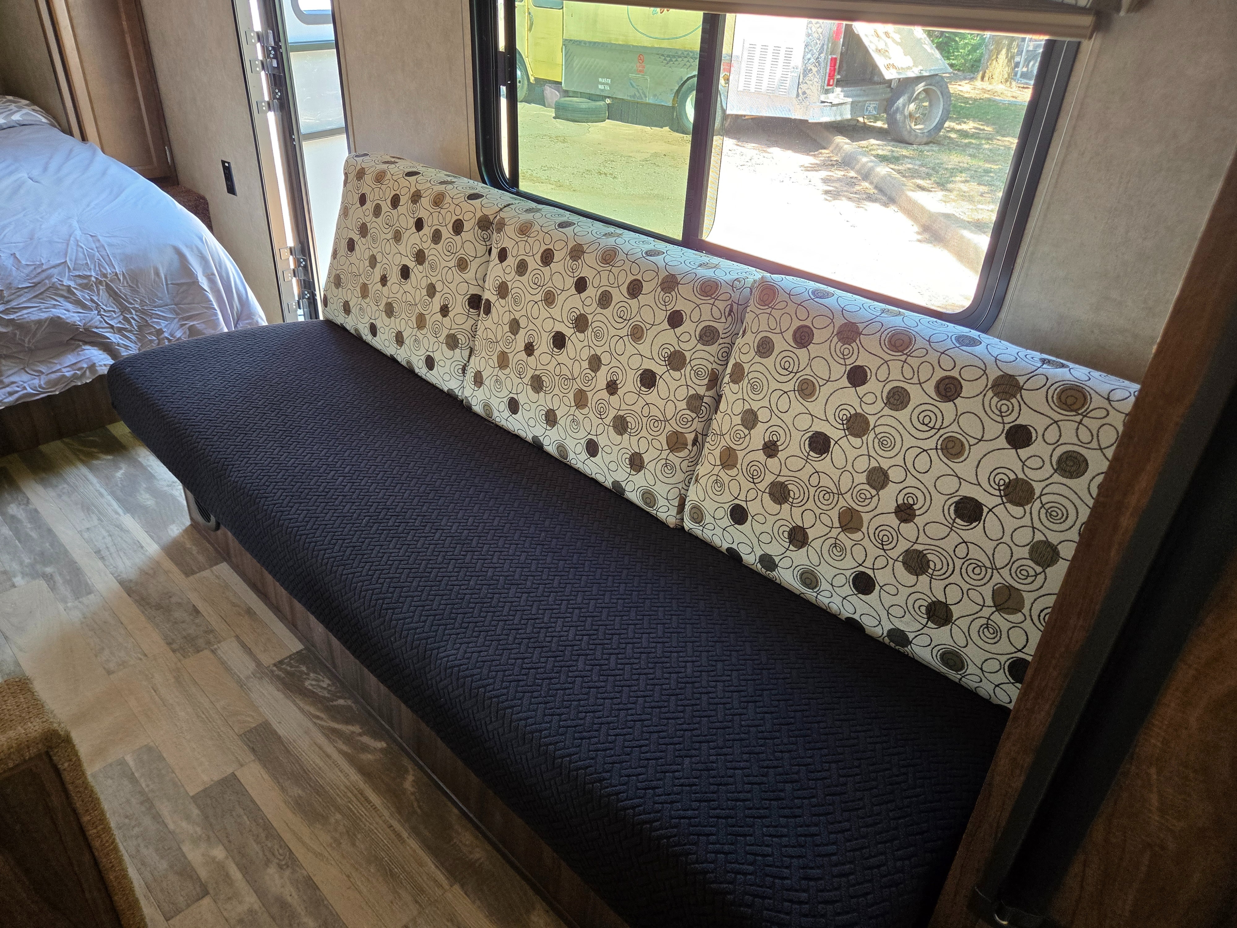 Inside an RV rental: a comfortable sofa with patterned cushions, a cozy bed, and a window view showing a truck outside.. Forest River Coachmen Classic 2018