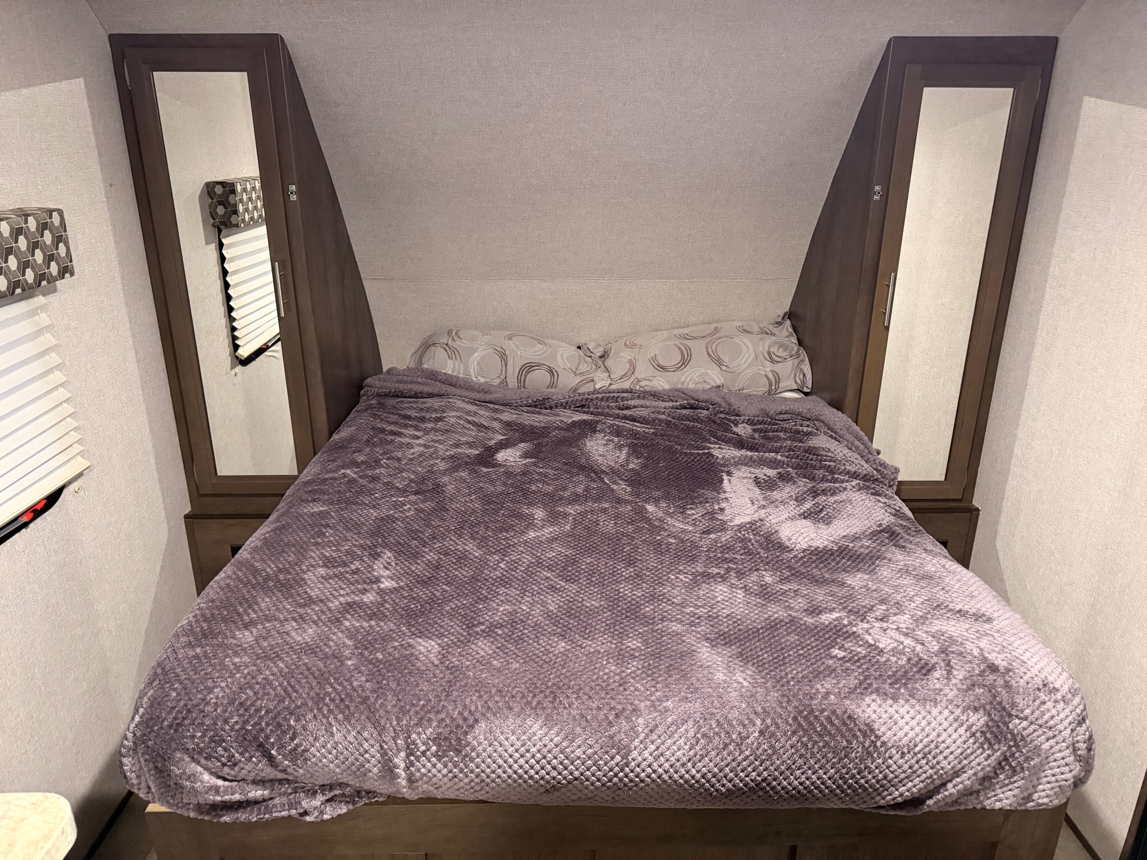 Comfortable rv rental bed featuring a plush purple blanket, patterned pillows, and built-in mirrored wardrobes.. Dutchmen Coleman Light LX 2020