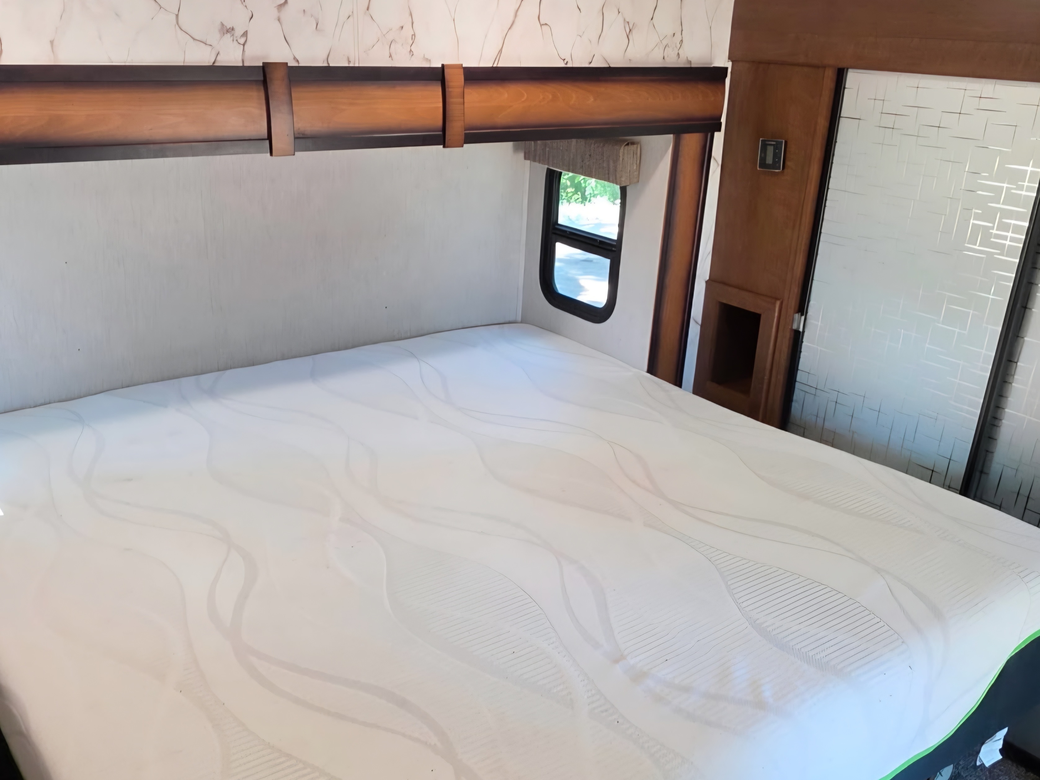 This RV rental bedroom features a large white mattress, wood headboard, and a window for natural light.. Heartland RVs Elkridge 2019