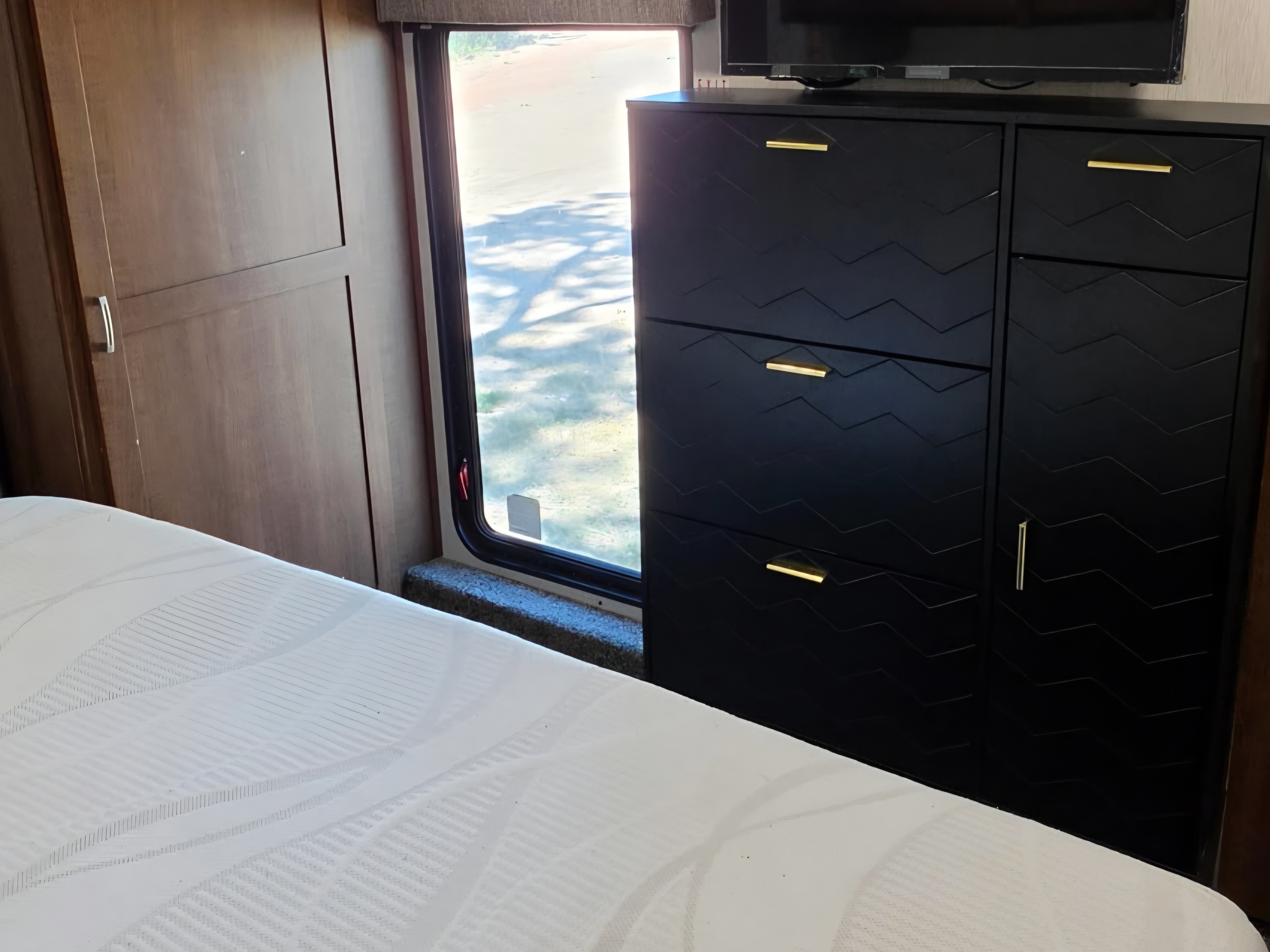 RV rental bedroom: white bed, window with outdoor view, and black zig-zag storage cabinet with gold handles.. Heartland RVs Elkridge 2019