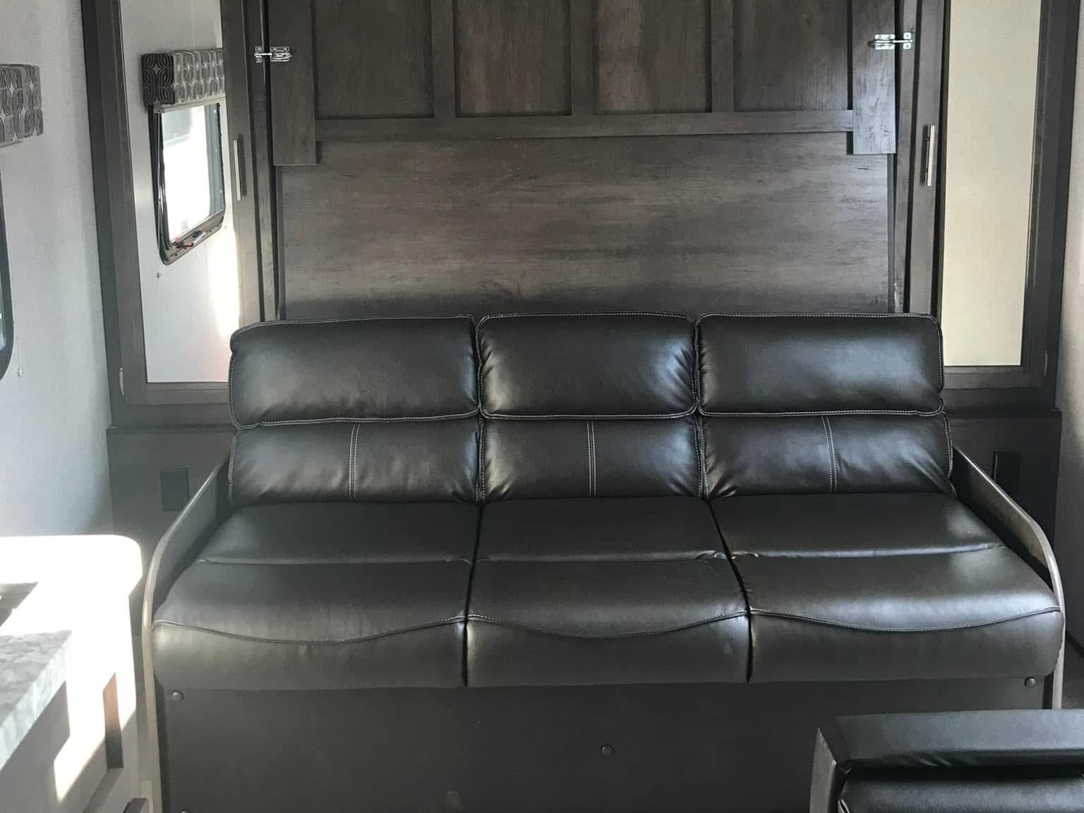 Experience comfort in this RV rental! A spacious dark sofa sits before wood paneling, offering a cozy interior living space.. Dutchmen Coleman Light LX 2020