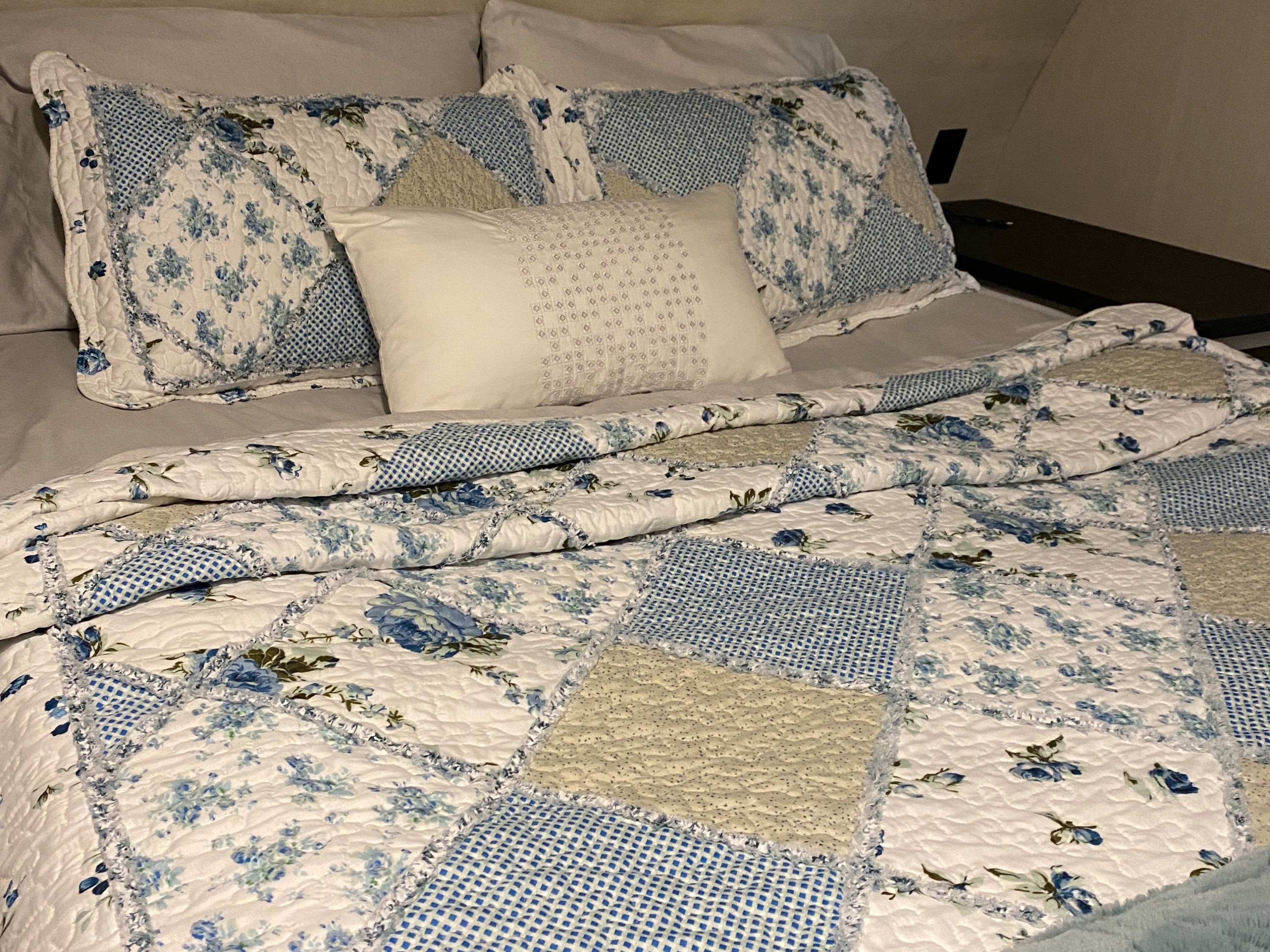 Cozy RV rental bedroom featuring a bed with a blue and white floral patchwork quilt and a soft blue blanket.. Forest River Vibe 2021