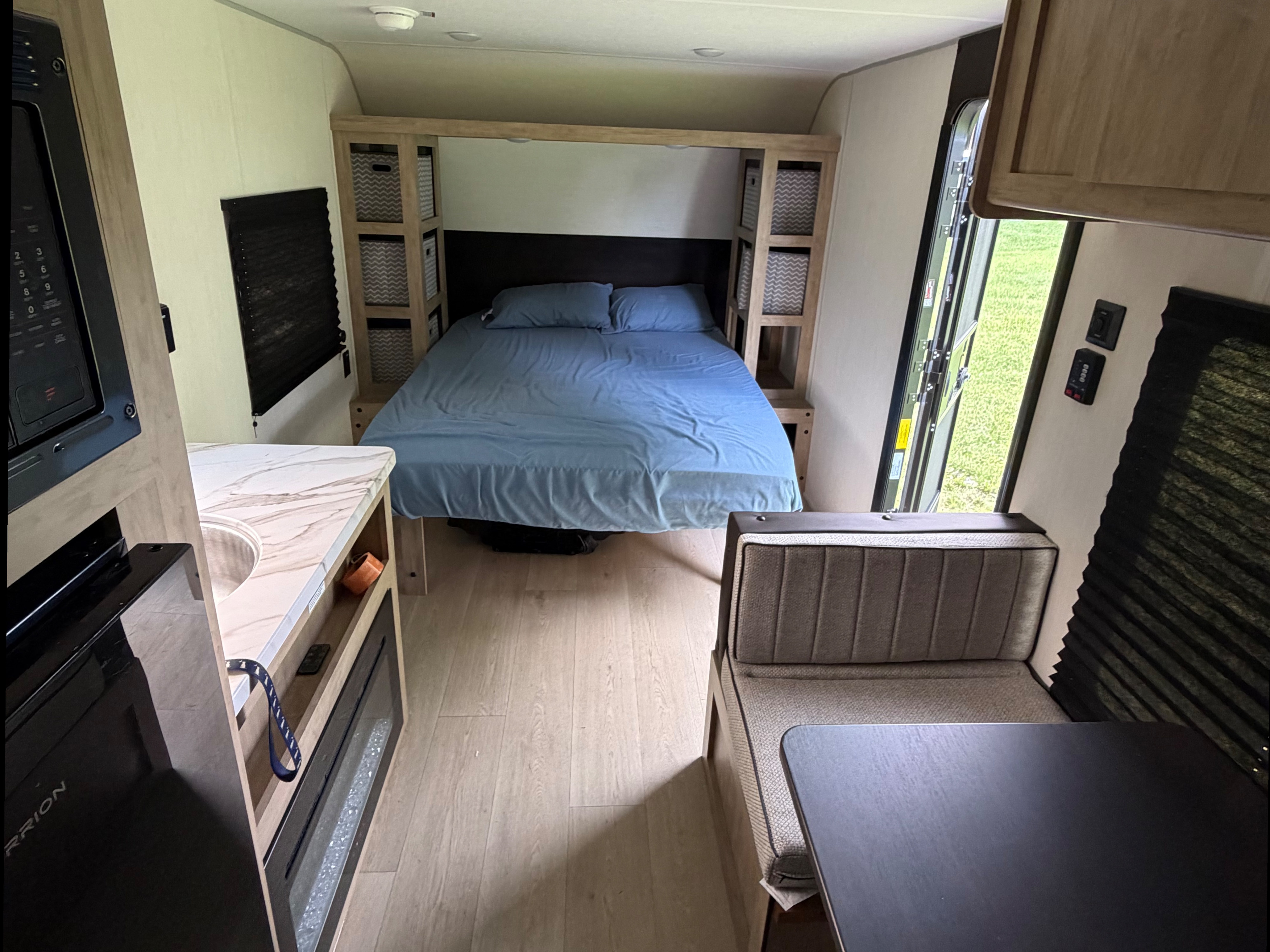 RV rental interior: cozy bedroom with blue bed, kitchen with microwave/sink, and dining booth in a compact living space.. Forest River Cherokee Wolf Pup 2026