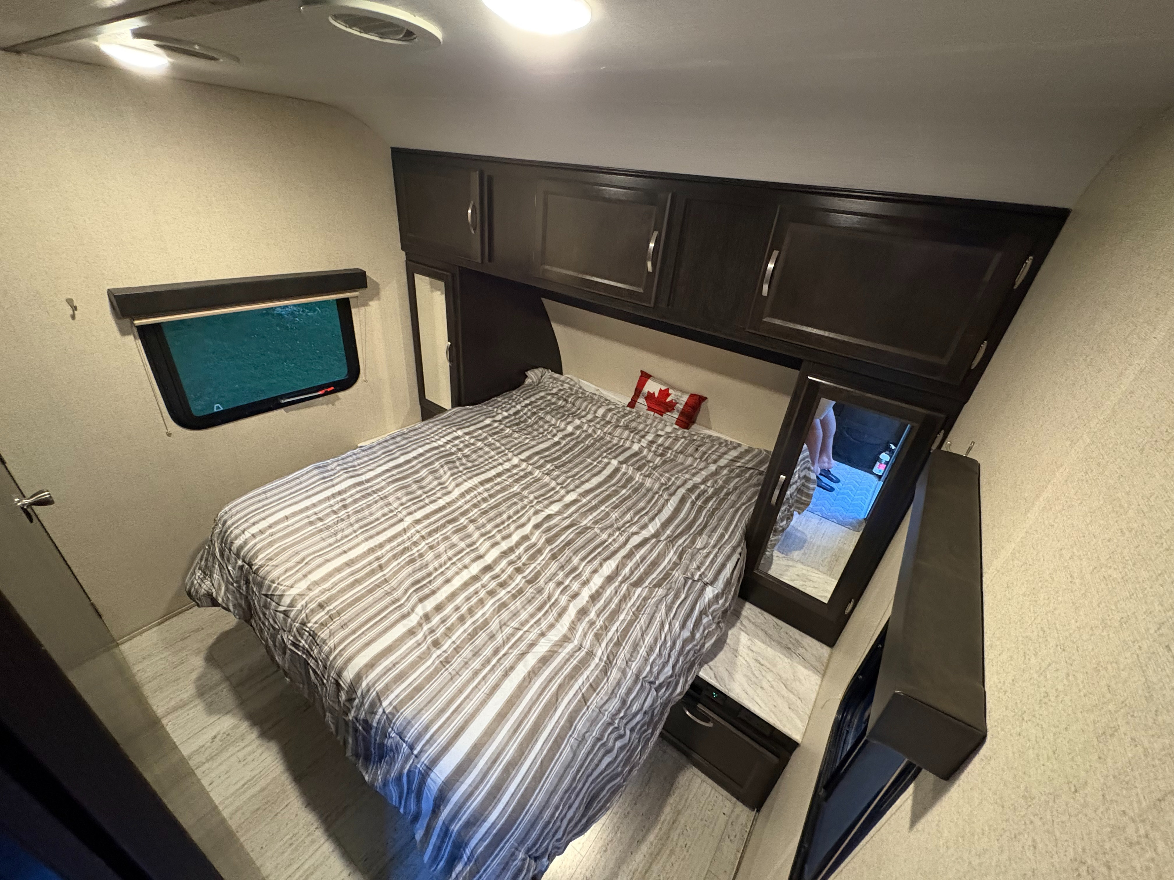 RV rental bedroom: striped bed, dark cabinets, window, and a mirror visible on the right, providing a cozy sleeping space.. Coachmen Northern Spirit 2454BH 2019