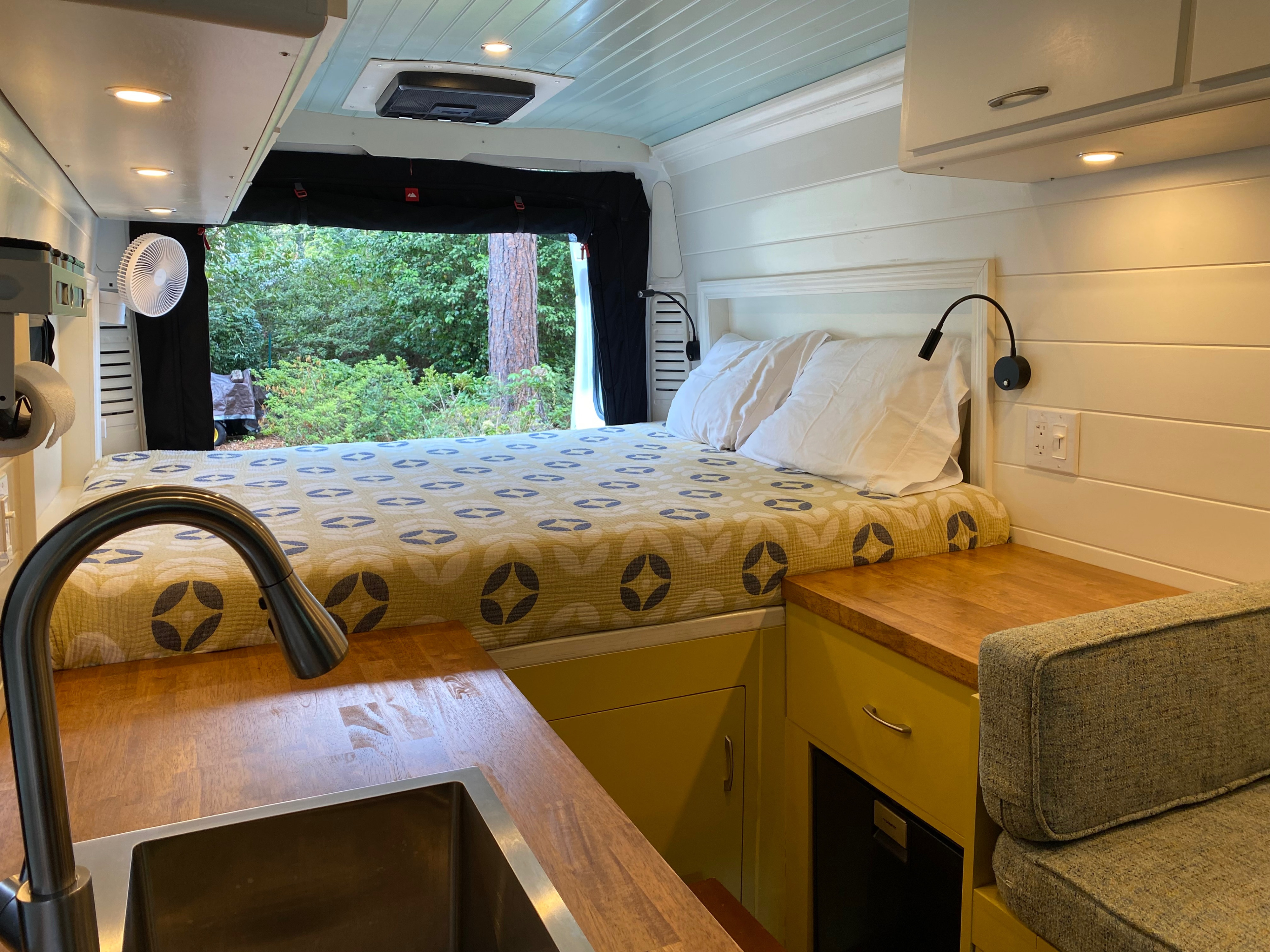 Bright RV rental interior: comfy bed, kitchen with sink & wood counter, cozy seating, and outdoor views.. Dodge Ram Promaster 3500 Hightop 2021