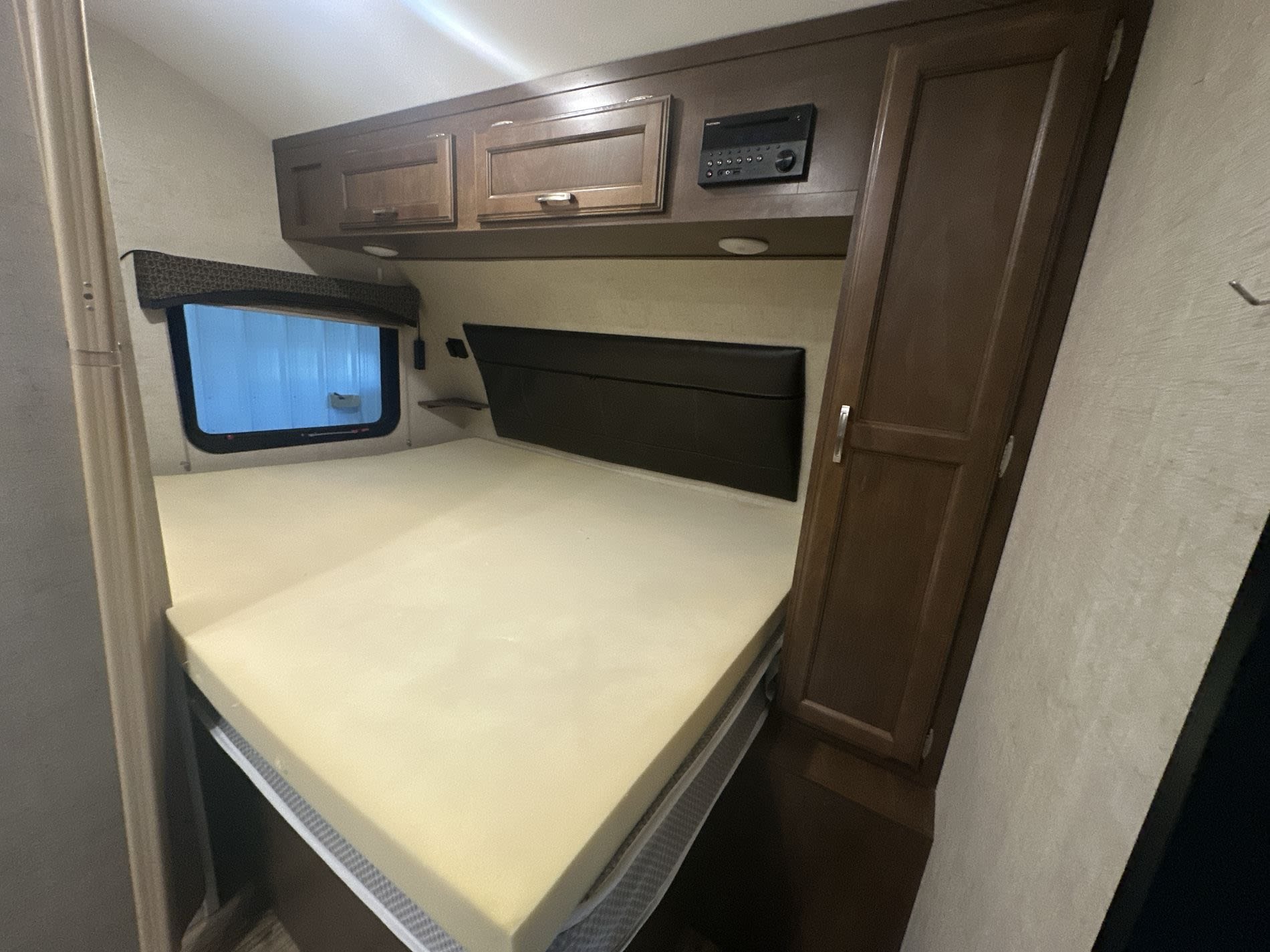 RV rental bedroom setup with a large bed, brown wooden cabinets, entertainment system, and window, perfect for your next trip.. Venture RV Sonic 170 VBH 2017