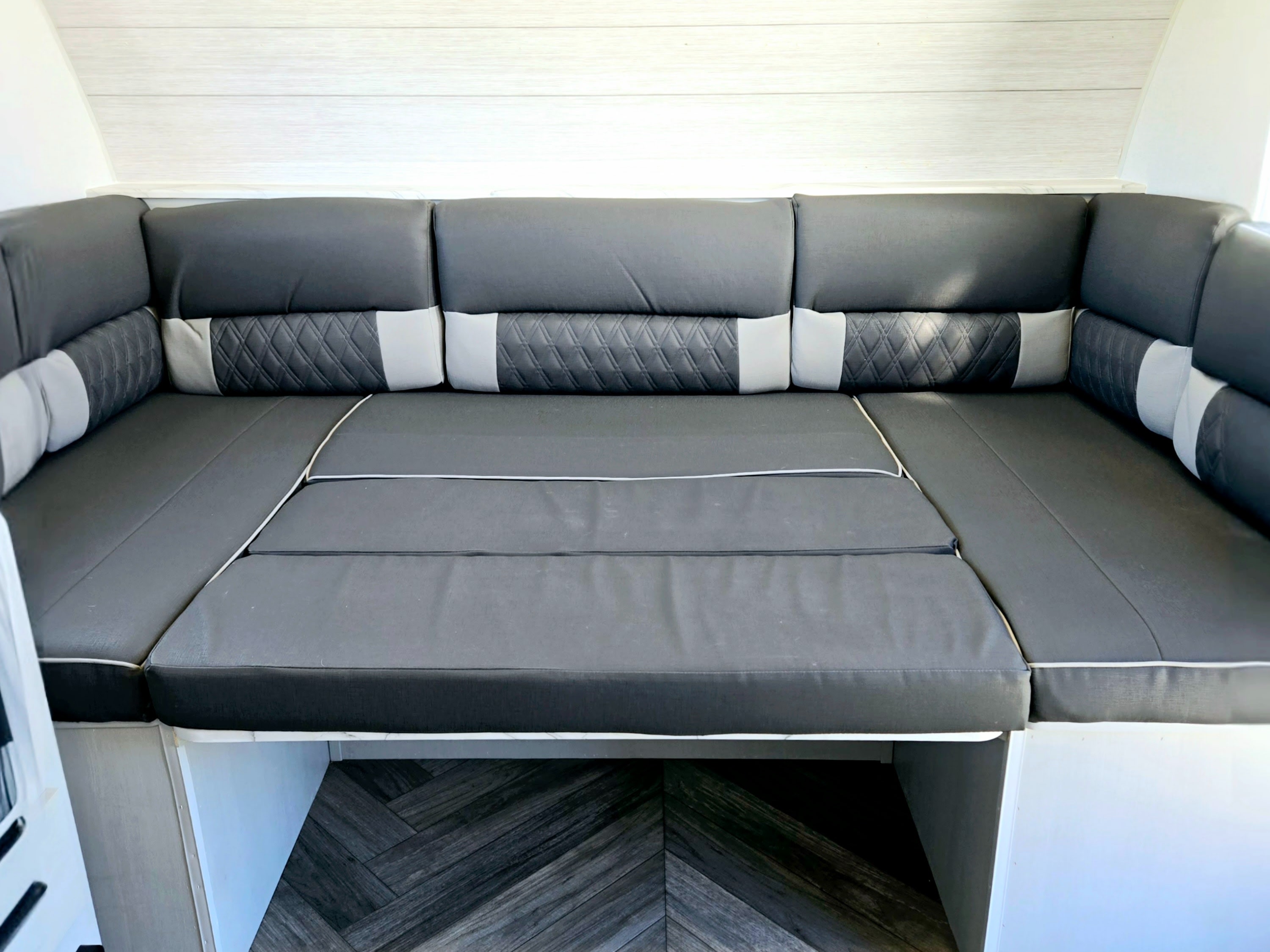 RV rental interior features versatile grey U-shaped seating with accent pillows, convertible into a bed, and a stylish herringbone floor.. Forest River Wildwood FSX 2022