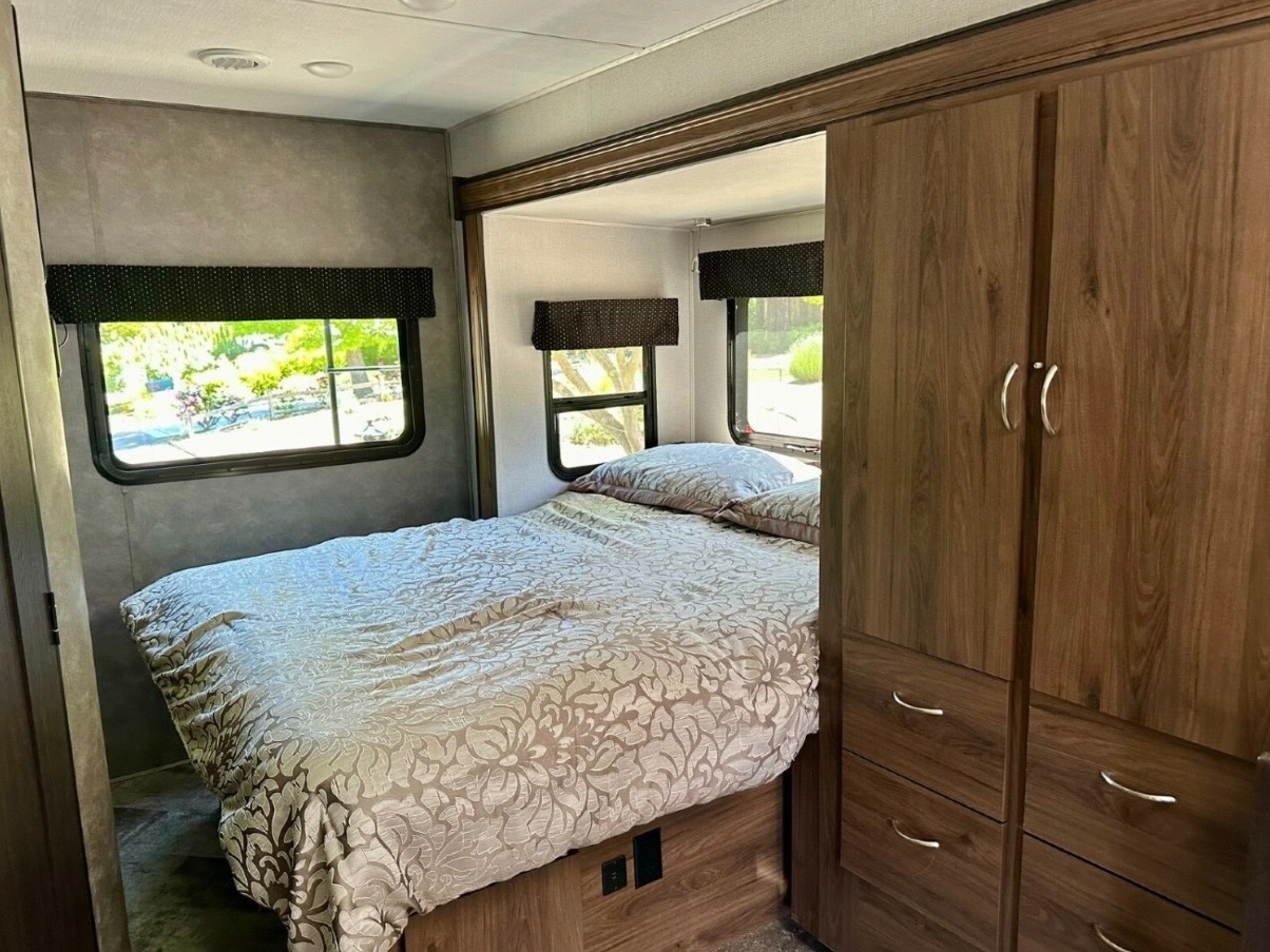 Cozy RV rental bedroom featuring a comfortable bed with patterned bedding, windows with blinds, and a built-in wardrobe.. Forest River Mercedes 2019