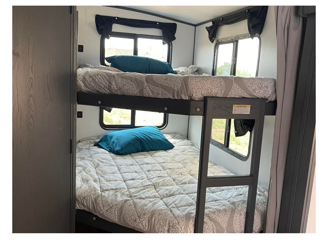 Family-friendly RV rental featuring cozy bunk beds with teal pillows & patterned bedding, plus scenic window views.. Keystone RV Bullet Ultra Lite 2022