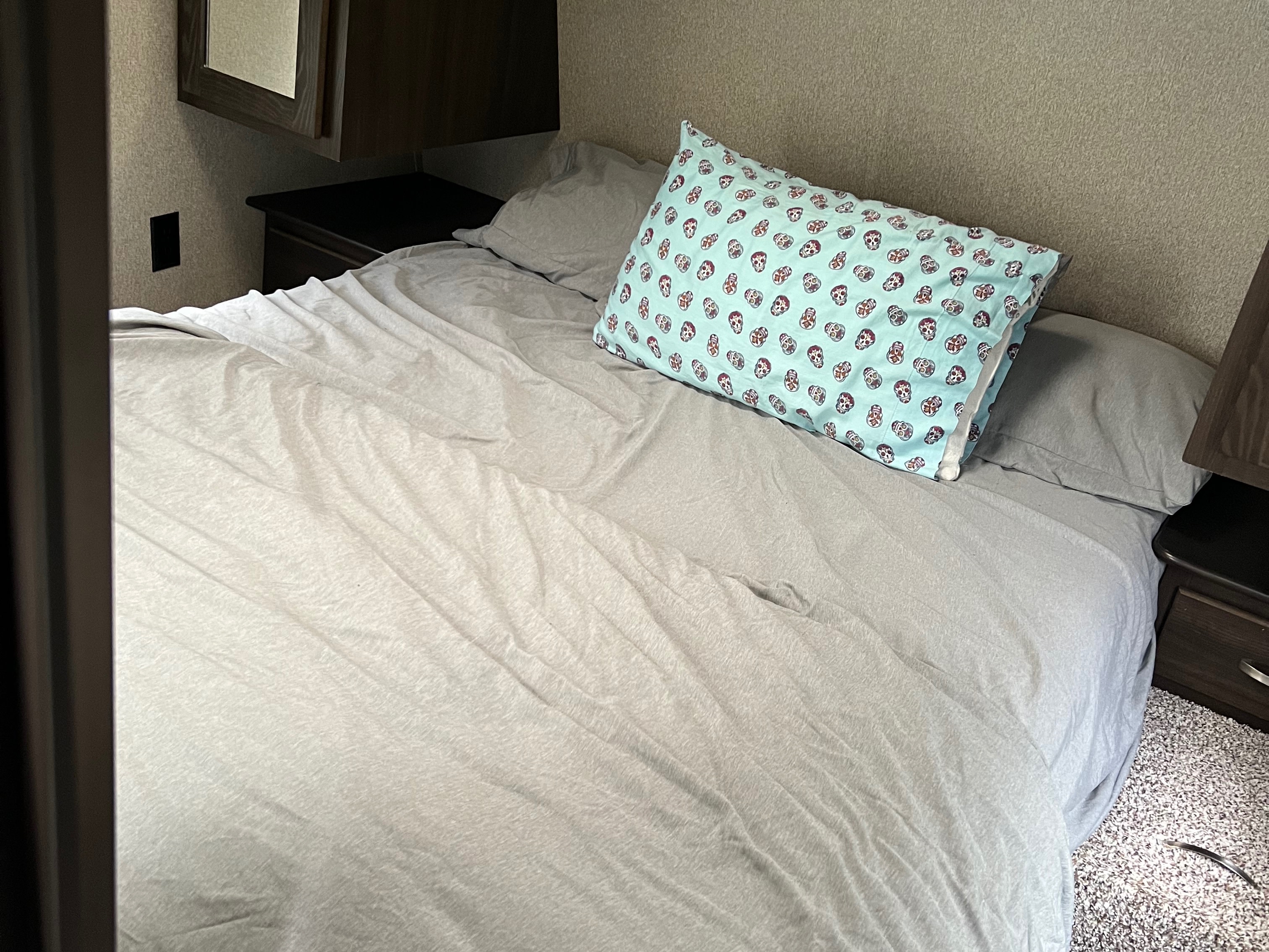 Cozy RV rental bedroom features a bed with light grey bedding and a blue pillow adorned with skull patterns.. Keystone RV Springdale Eco-Lite 2018