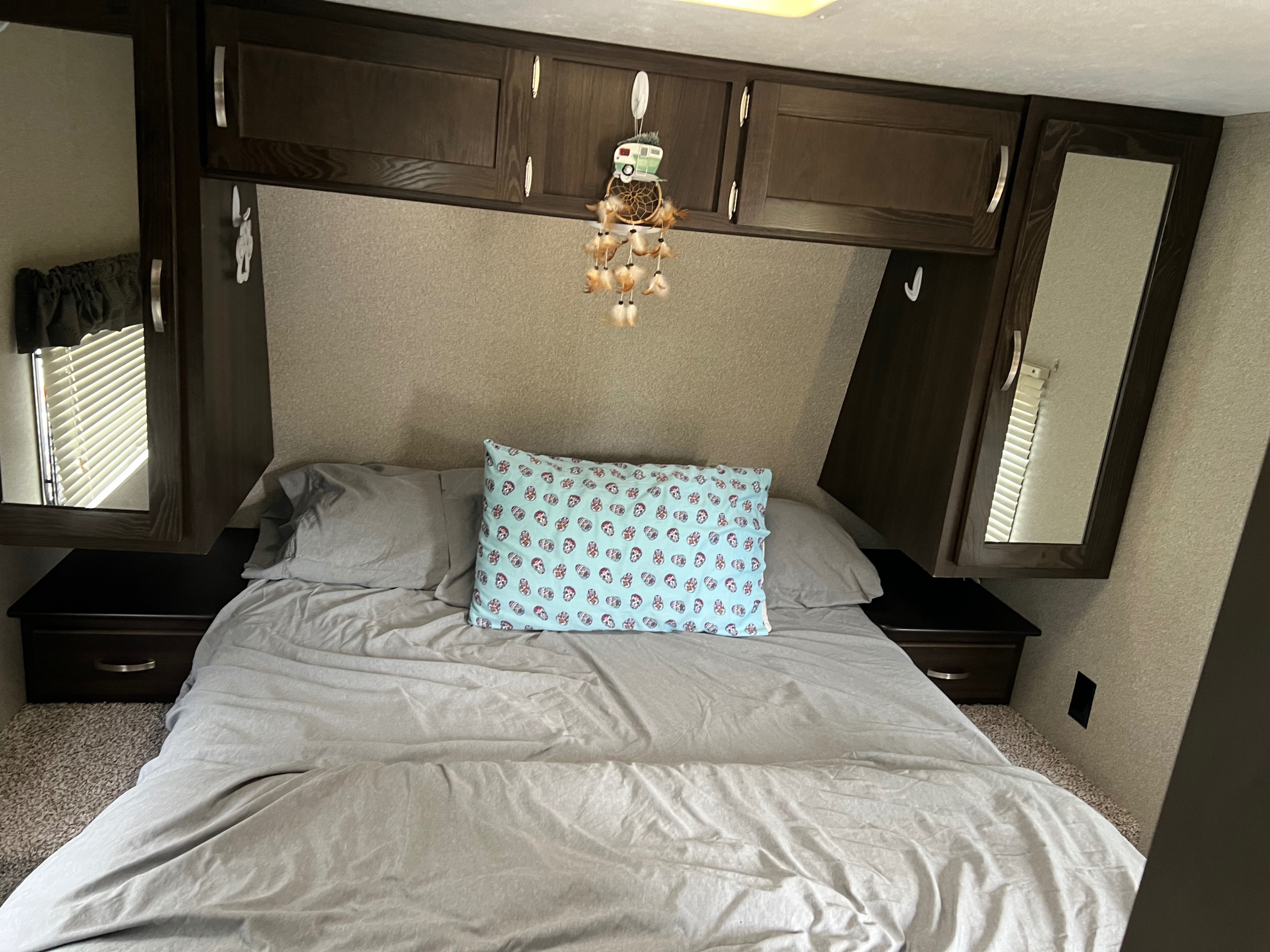Cozy RV rental bedroom featuring a bed with gray sheets and patterned pillow, dark wood overhead cabinets, and mirrored storage.. Keystone RV Springdale Eco-Lite 2018