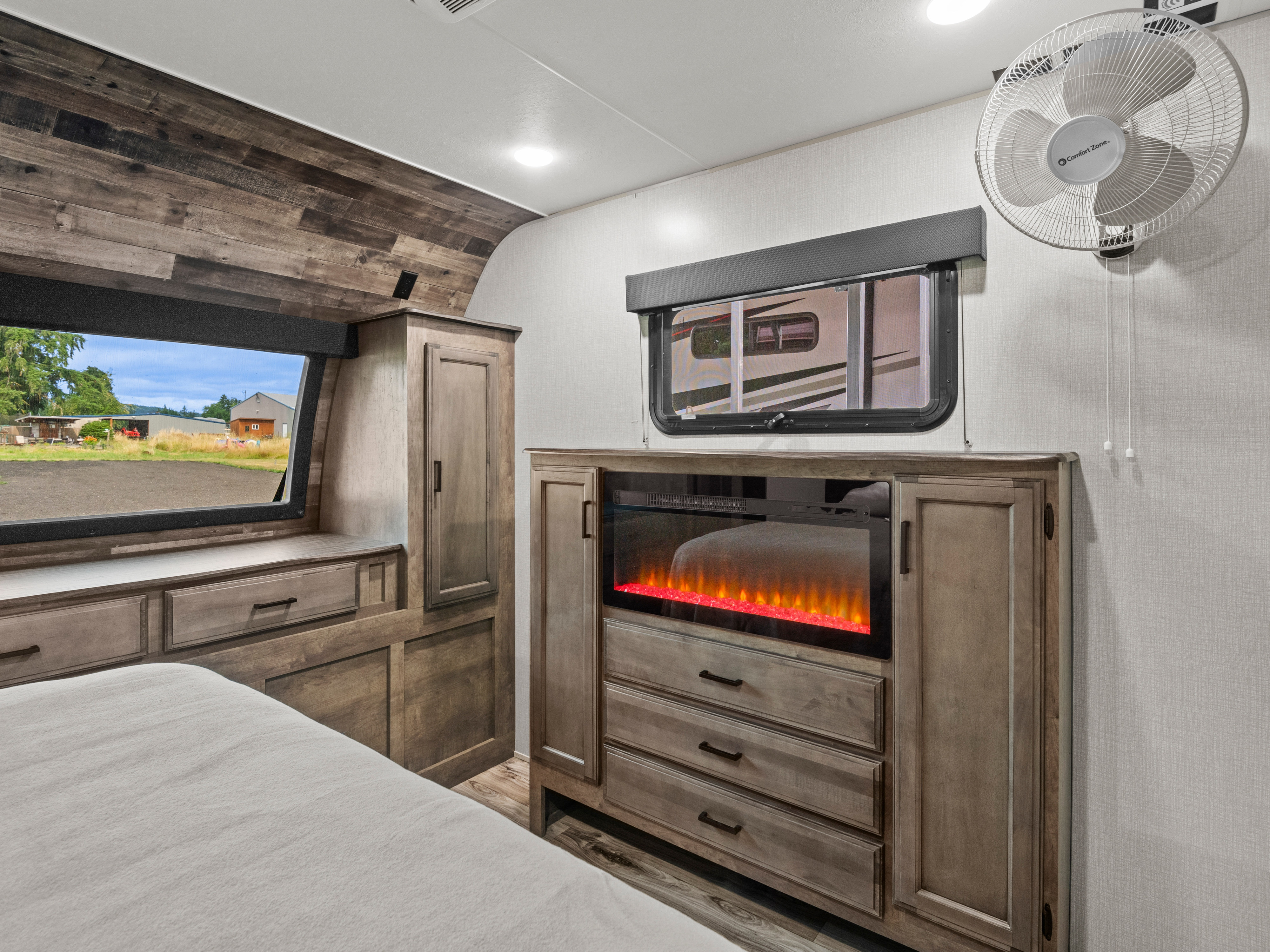 Modern rustic RV rental bedroom features a fireplace, built-in storage, a wall fan, and large windows with outdoor views.. Sport Trek Touring 2021