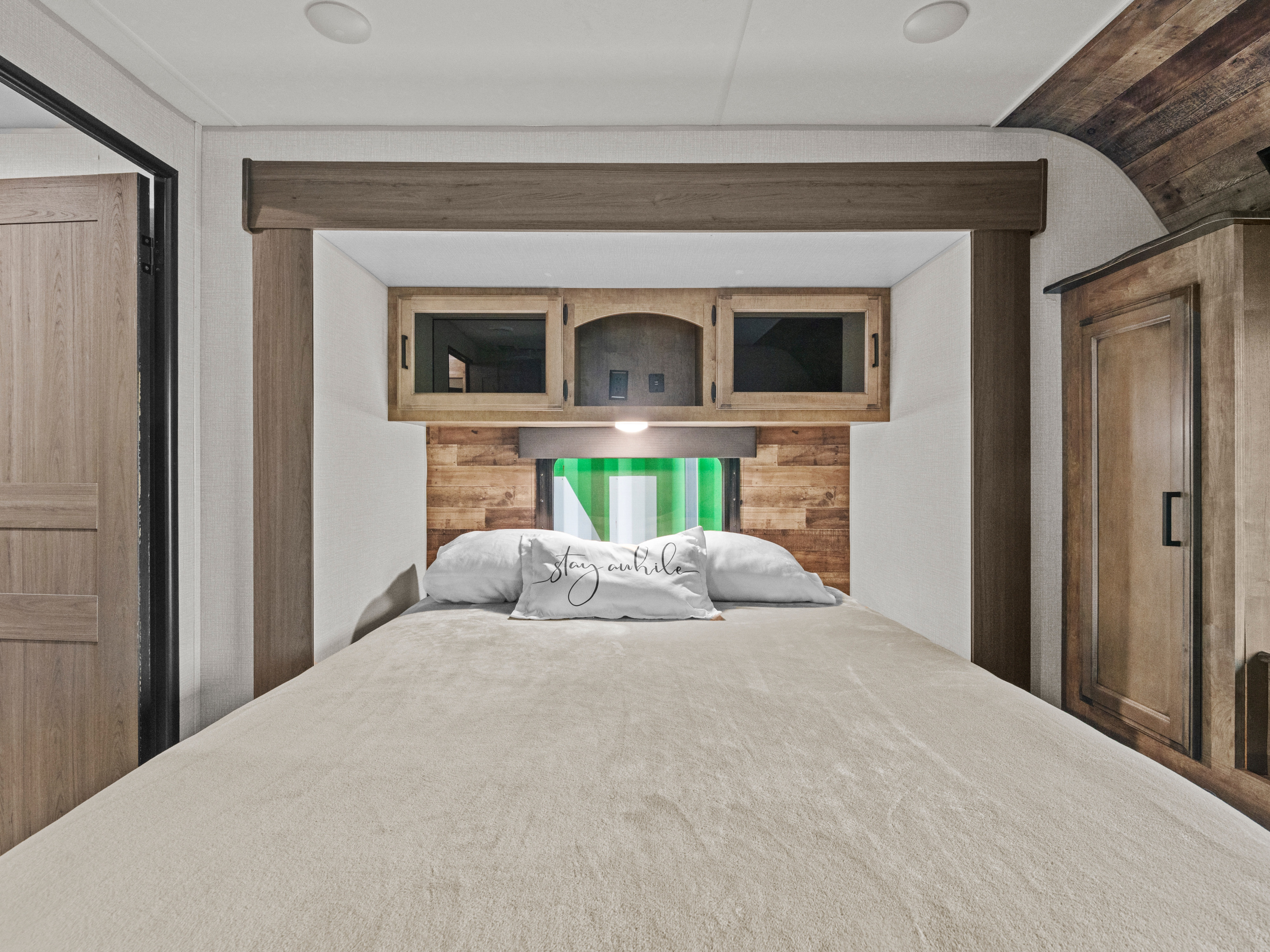 Cozy RV rental bedroom with a comfy bed, wooden accents, overhead storage, and a "Stay Awhile" pillow.. Sport Trek Touring 2021
