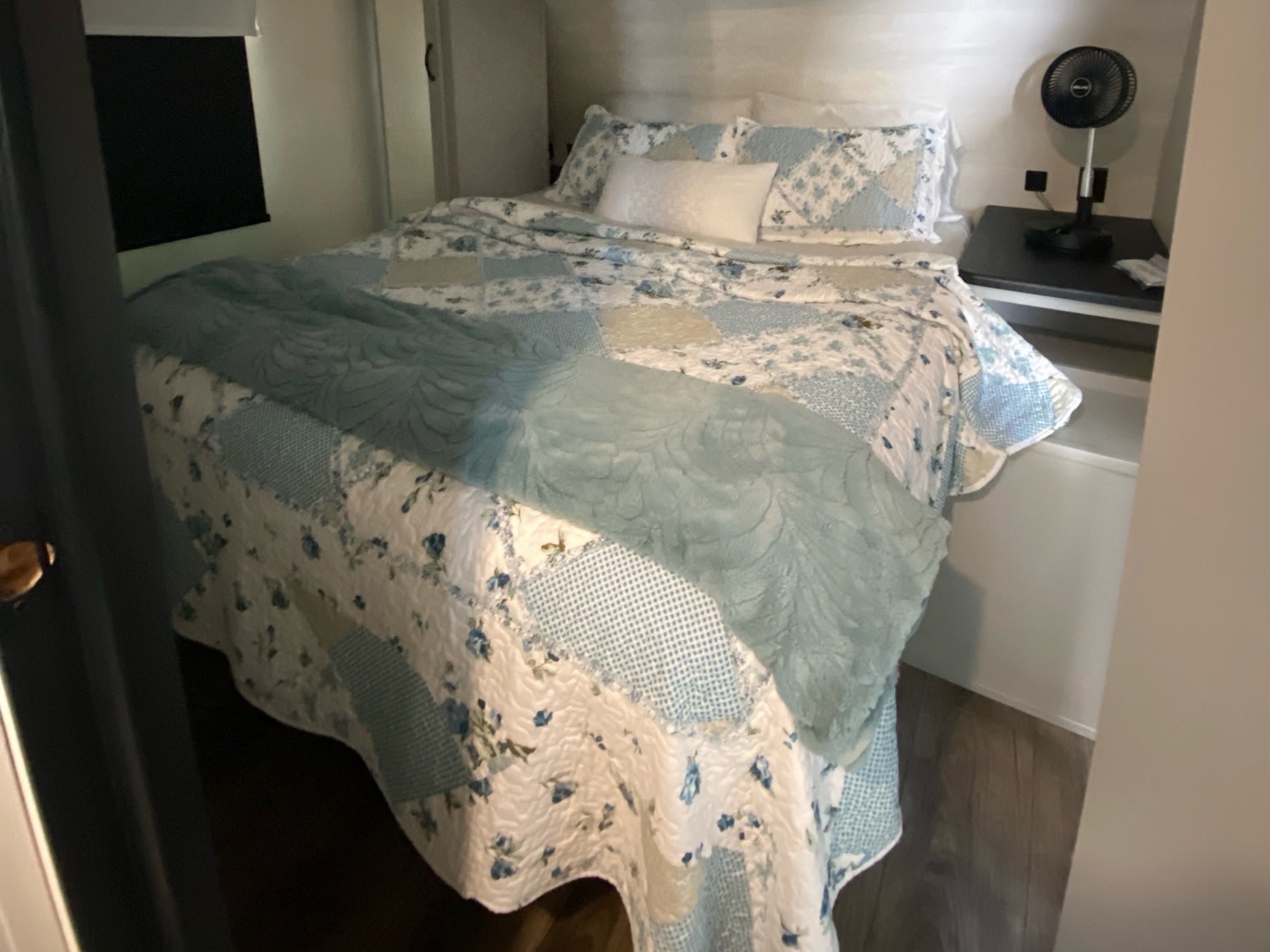 Relax in your RV rental's cozy bedroom. Features a comfortable bed with a blue floral quilt and a bedside fan.. Forest River Vibe 2021