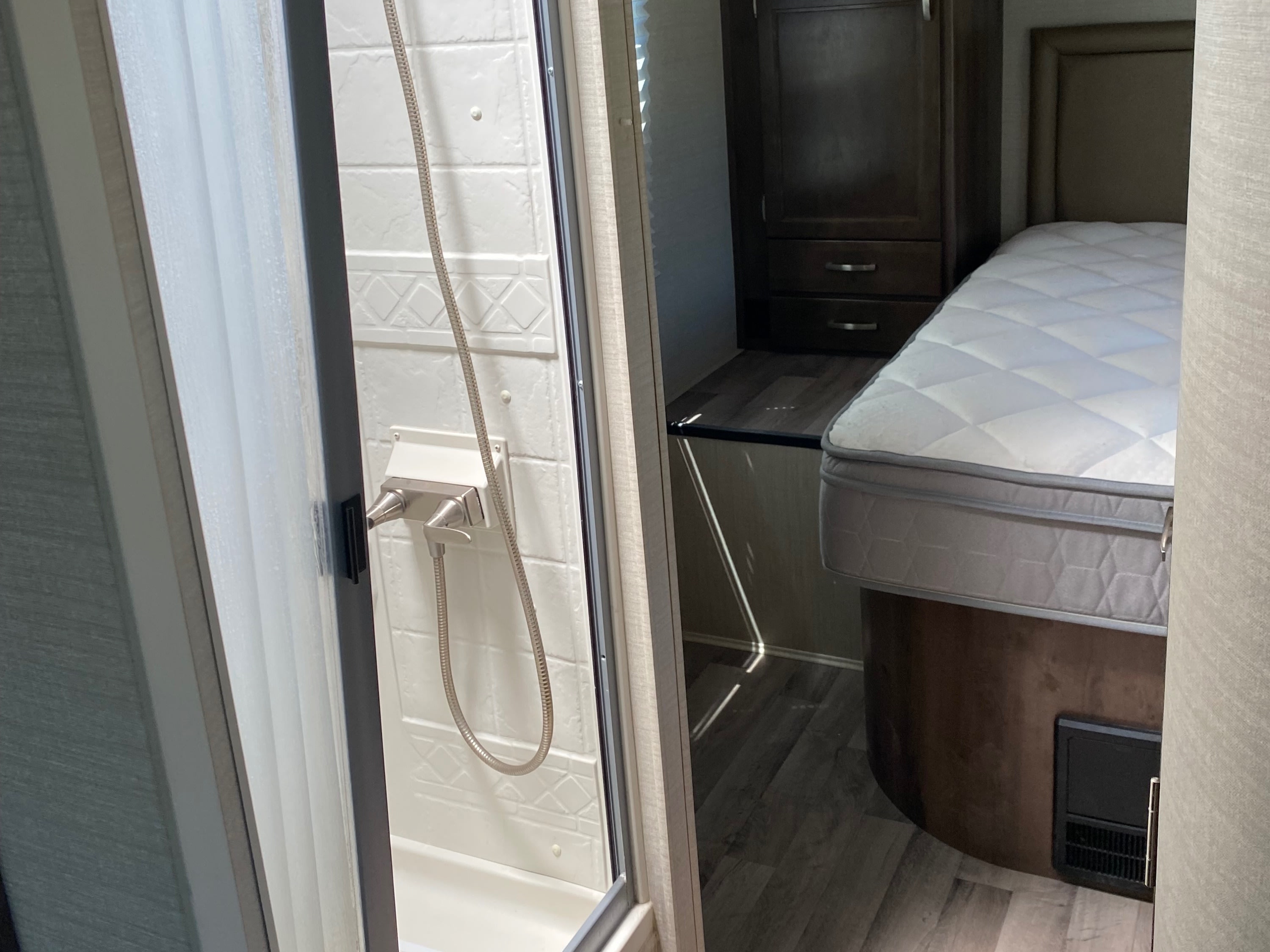 Inside this modern rv rental, a compact interior features a shower stall with a curved glass door and a bedroom area.. Jayco Redhawk 2019