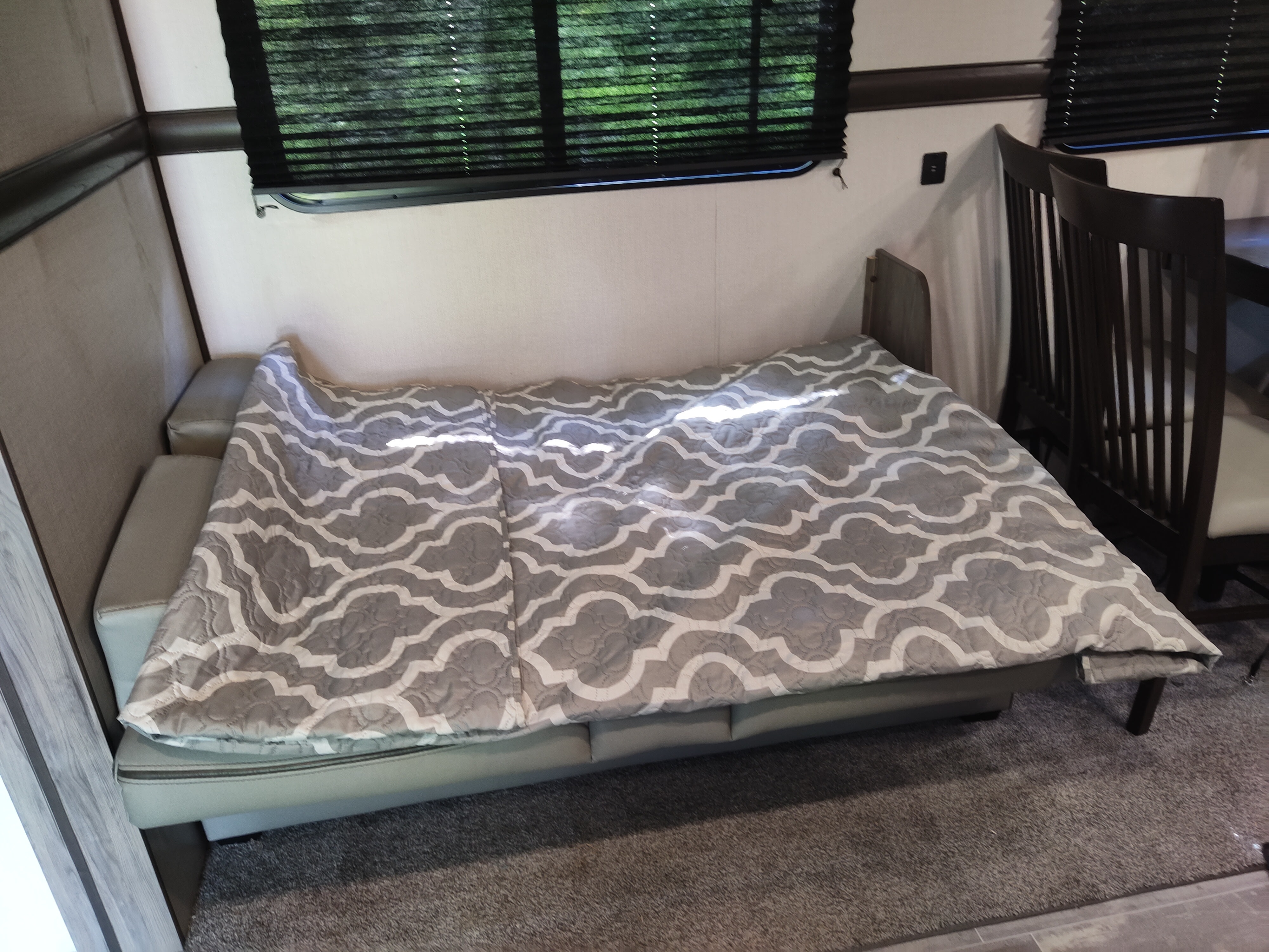 RV rental interior: A cozy convertible couch/bed with a patterned blanket, window with blinds, and dining chairs.. Zinger 280RB 2020