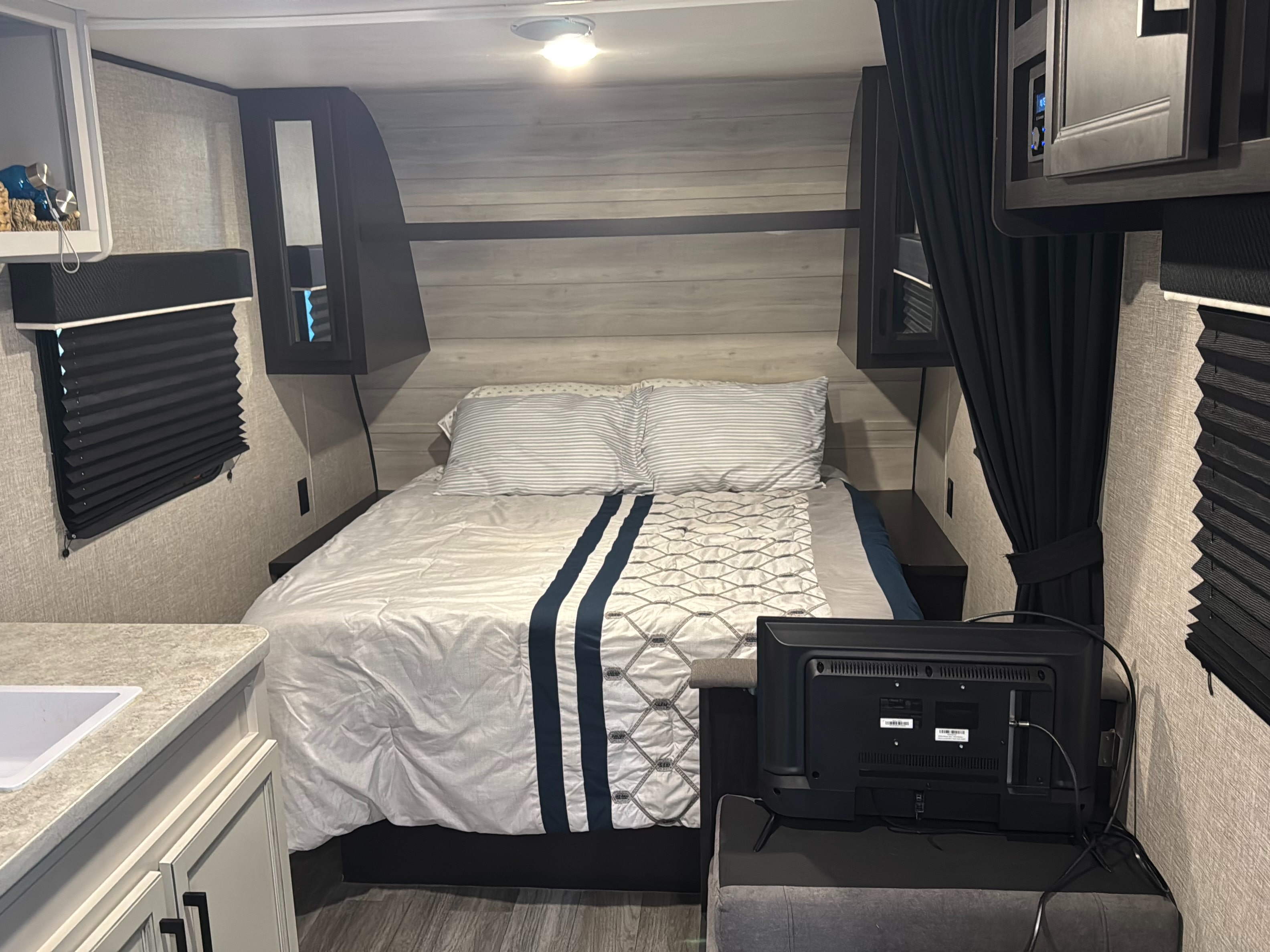 Cozy RV rental bedroom showing a made bed with blue accents, overhead storage, window blinds, and a TV at the foot.. Jayco Jay Flight SLX 2022