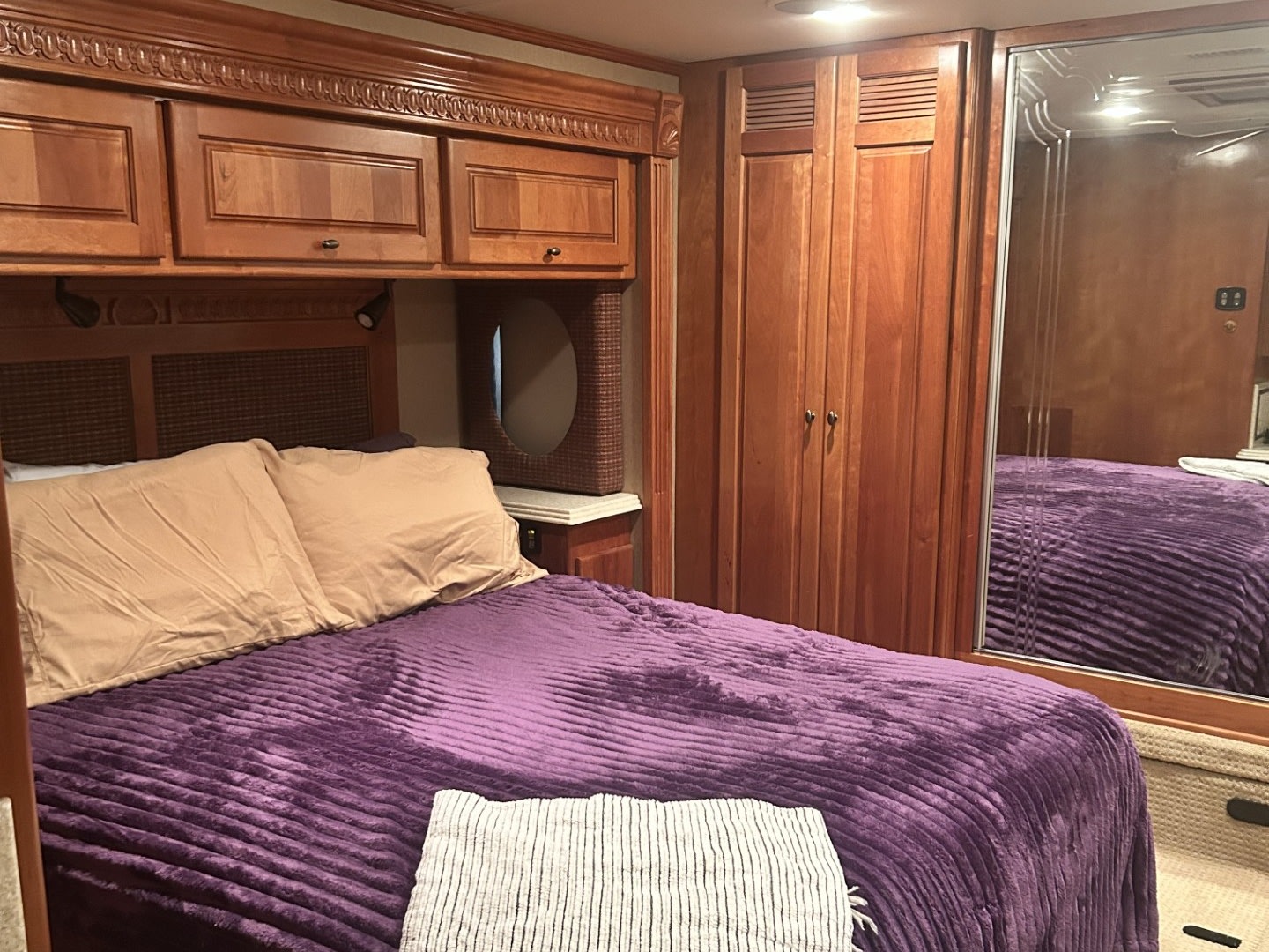 Cozy RV rental bedroom with a bed featuring a purple blanket, overhead wood cabinets, and a full-length mirror.. Monaco Dynasty 2008