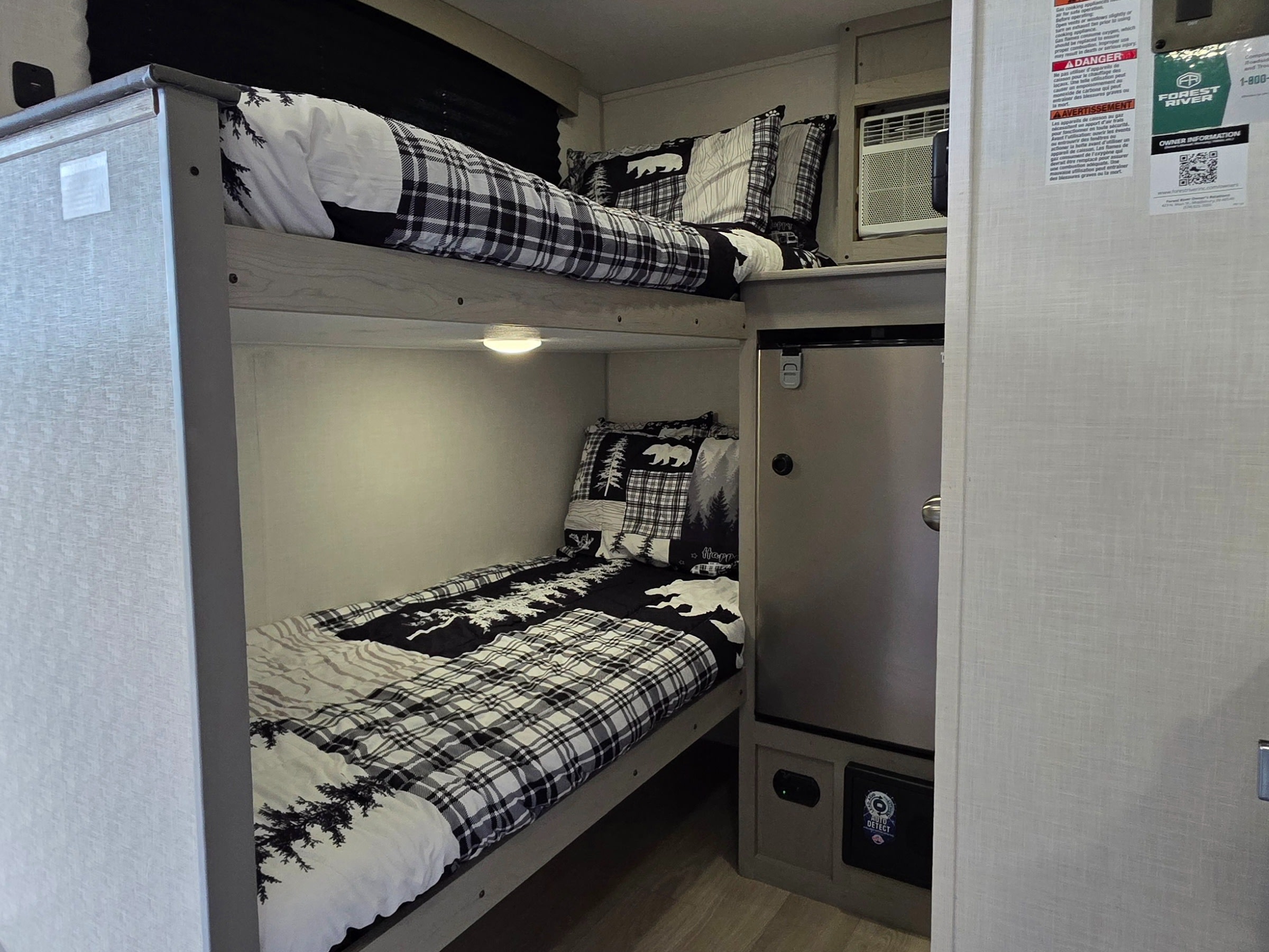 Cozy RV rental bunk beds with black & white bear and plaid bedding, an AC unit, and mini-fridge for comfortable travel.. Forest River 12BH 2026