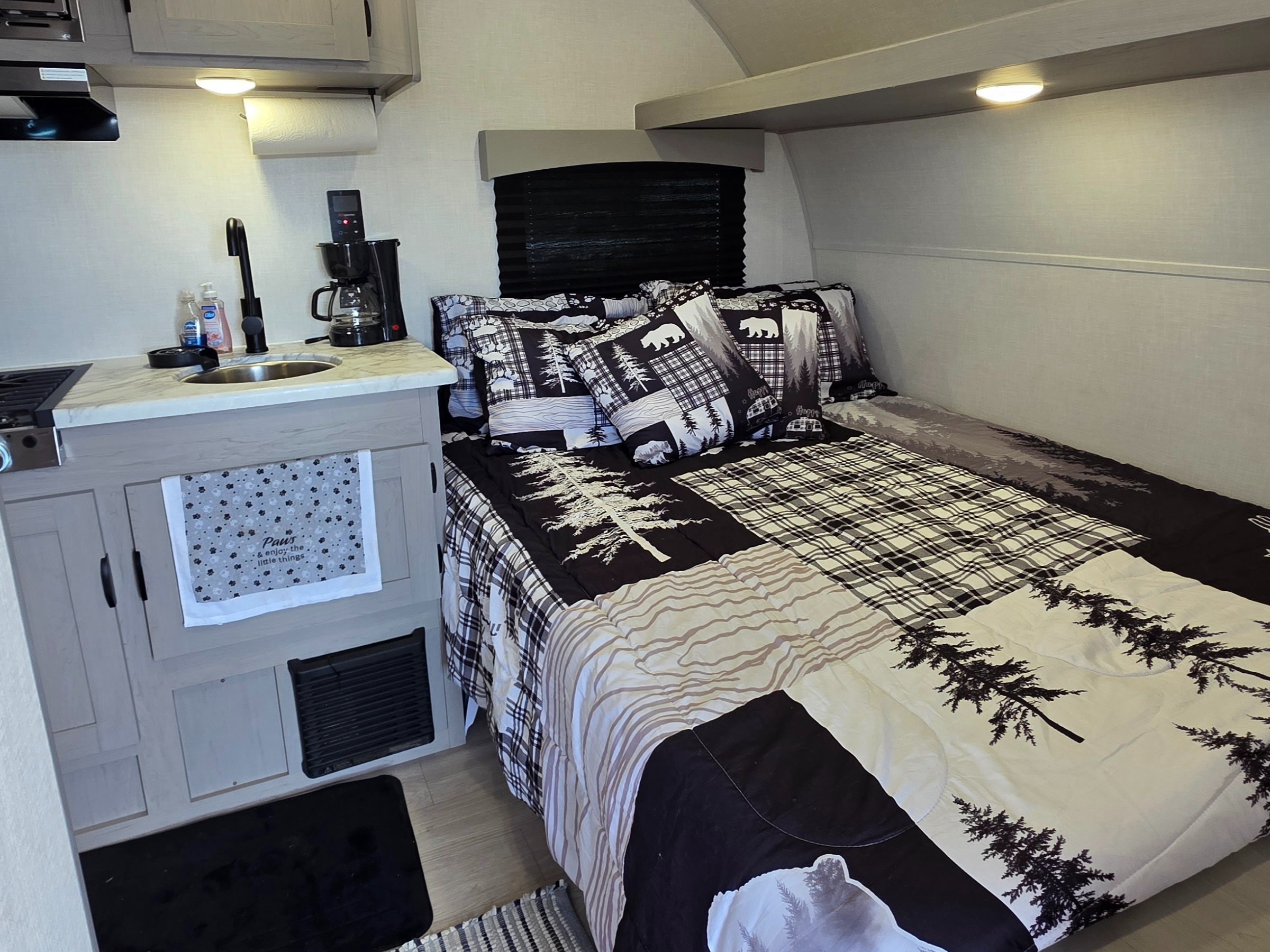 Cozy rv rental interior: compact kitchen with sink, coffee maker, and bed with bear & tree themed bedding.. Forest River 12BH 2026