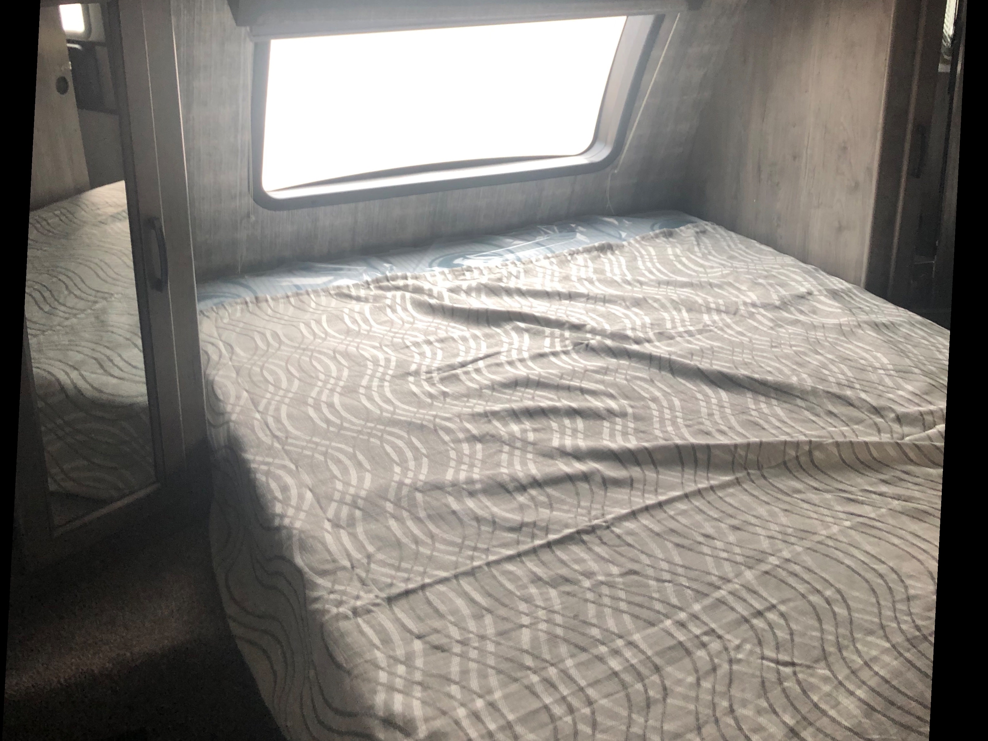 RV rental bedroom: a comfortable bed with patterned bedding, a bright window, and mirrored wardrobe reflect a cozy space.. Coachmen Apex 2019