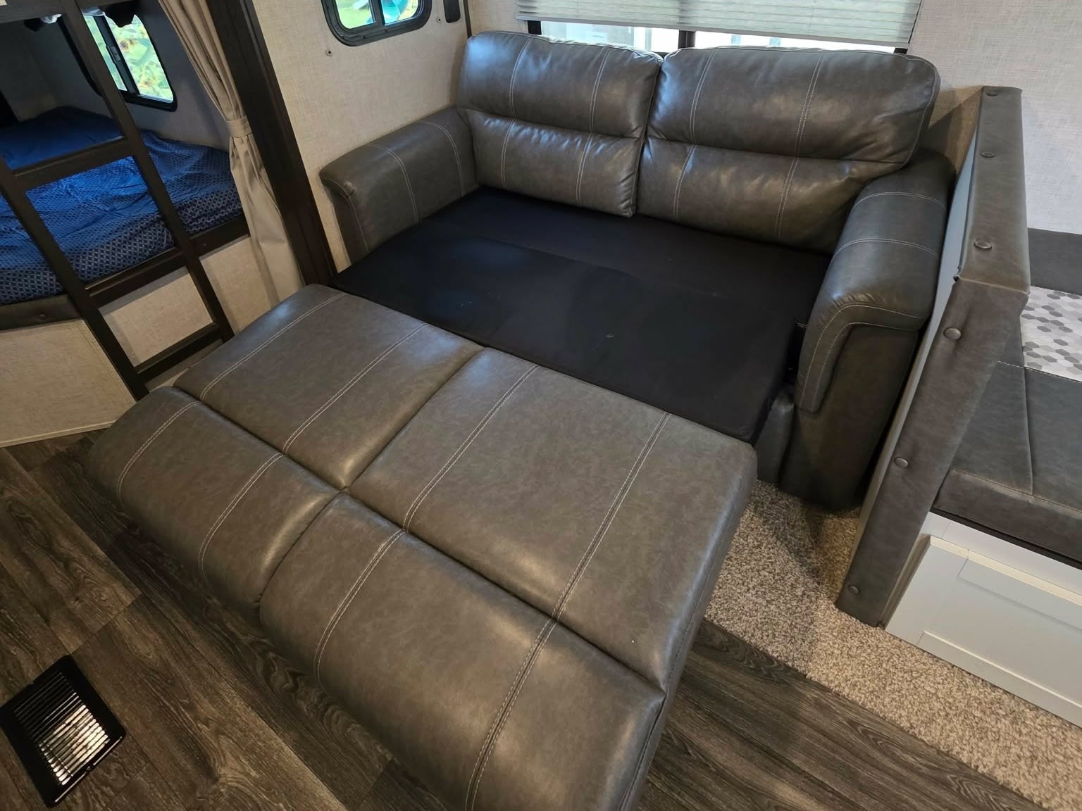 This RV rental features a gray sofa bed extended for sleeping, alongside bunk beds and a dining booth for comfortable living.. Keystone RV Bullet Ultra Lite 2021