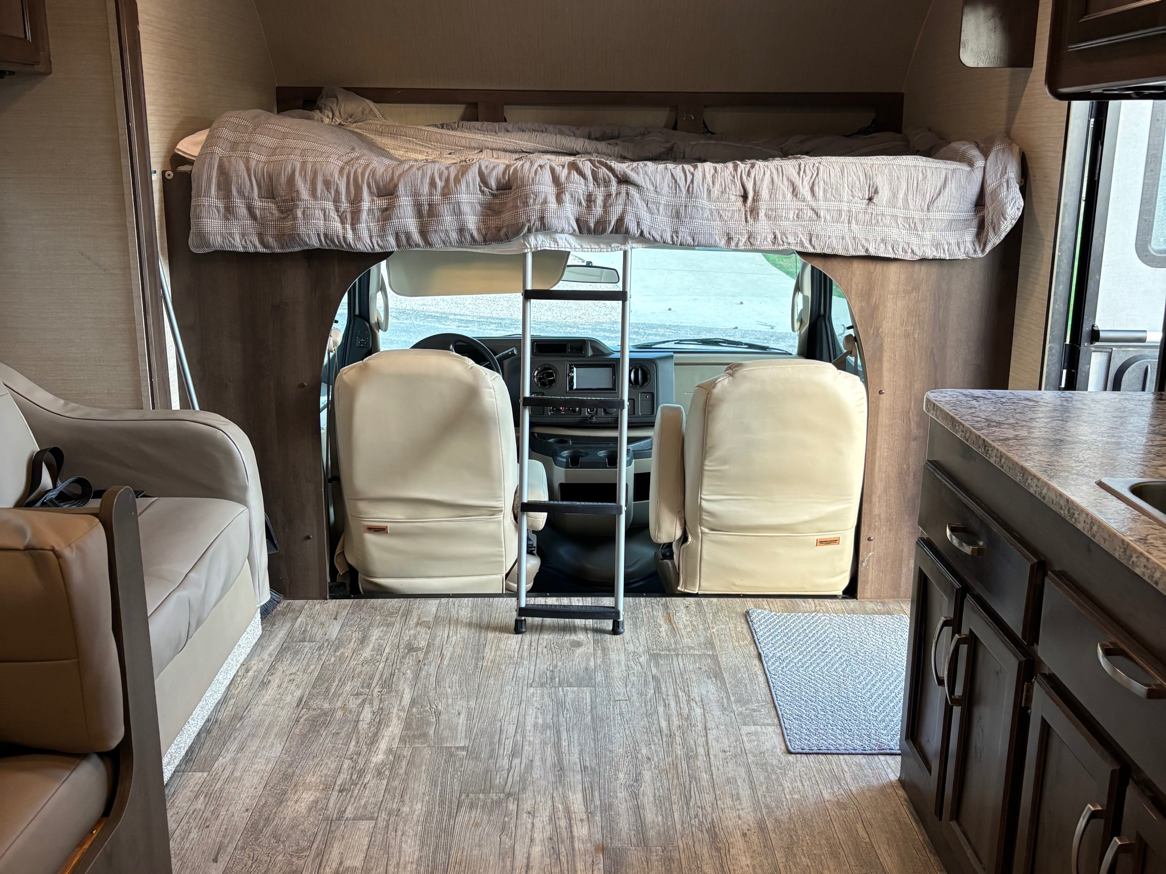 This rv rental features a cozy cab-over bed, driver's area, kitchen counter, and seating, offering comfort for travel.. Jayco Redhawk 2018