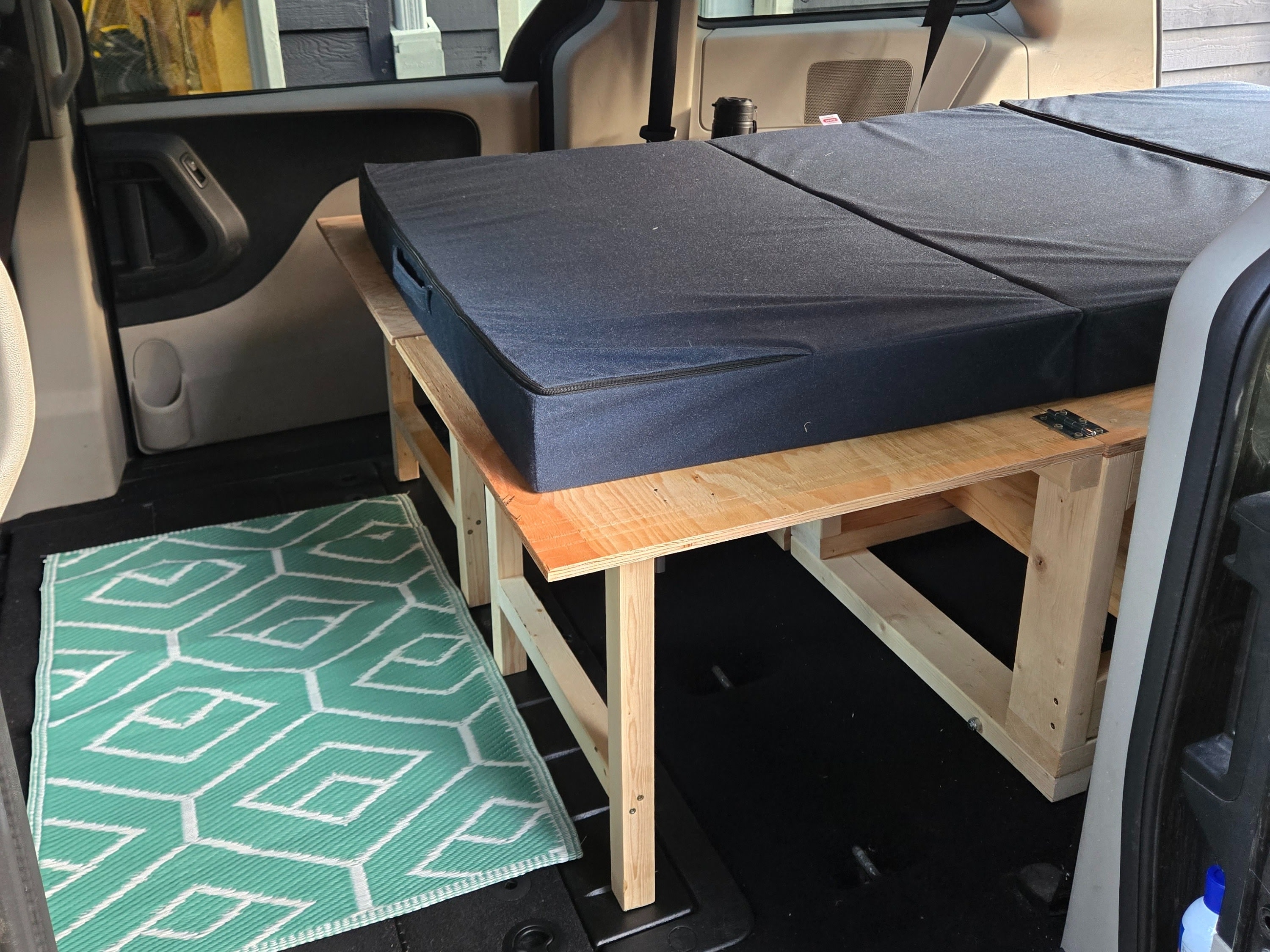 Inside a vehicle: a wooden sleeping platform with blue segmented cushions and a green patterned mat. Perfect for RV rental.. Dodge Grand Caravan 2014