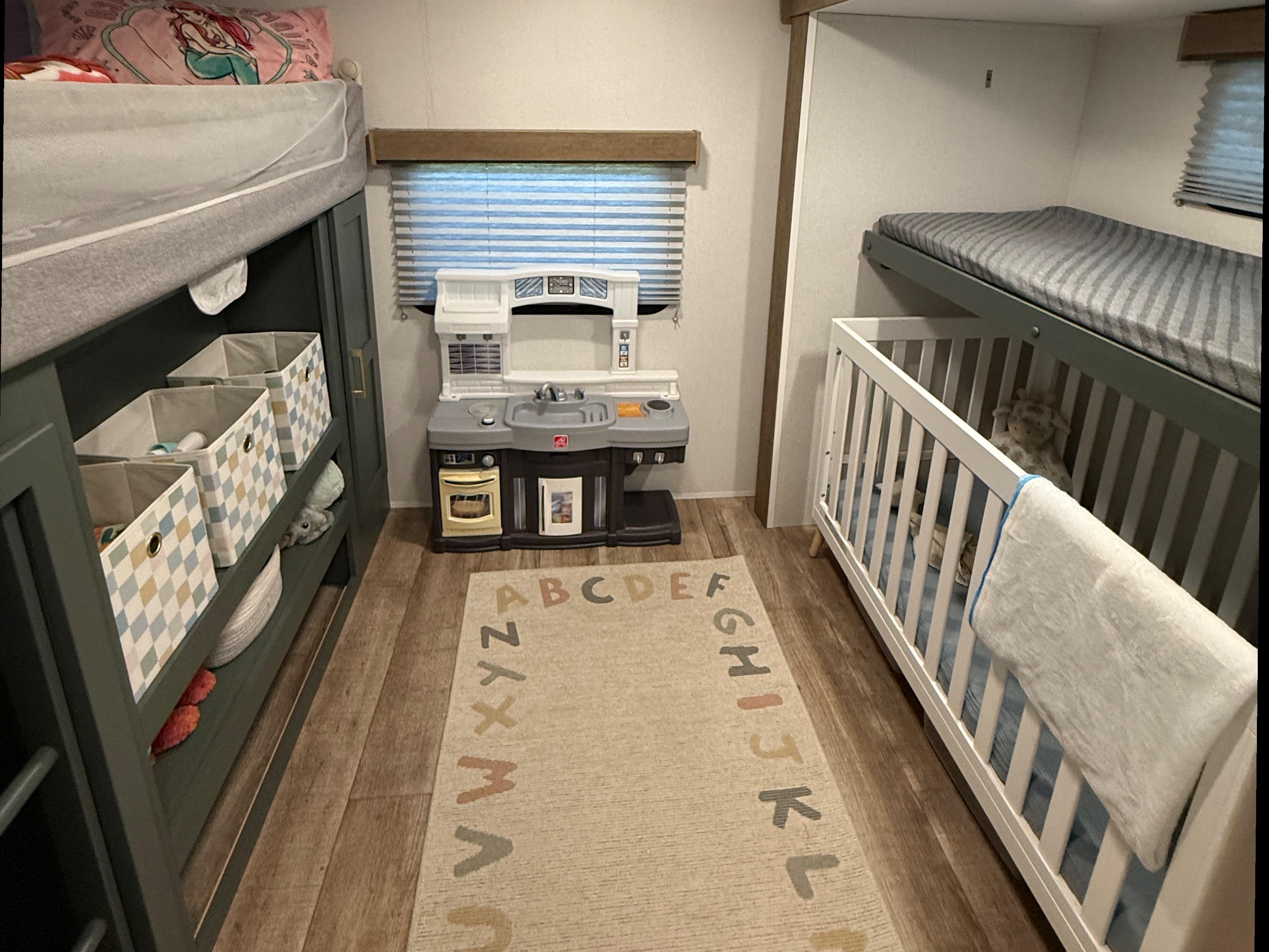 Cozy RV rental interior with bunk beds, a crib, and a play kitchen on an ABC rug, perfect for family adventures.. Heartland RVs Eddie Bauer 2026