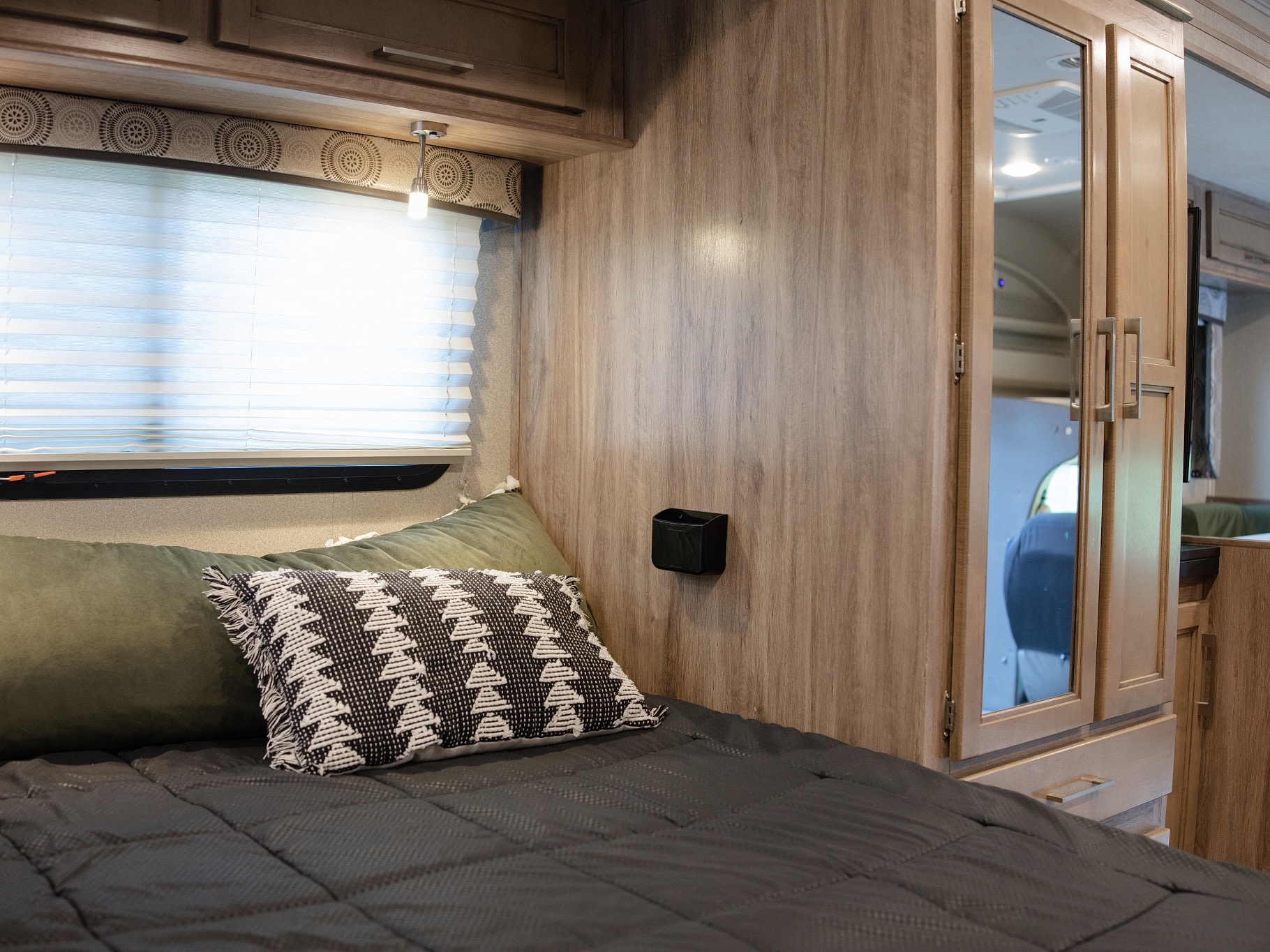 Comfortable RV rental bedroom with modern bedding, a window, overhead storage, and mirrored cabinets.. Entegra Coach Odyssey 2020