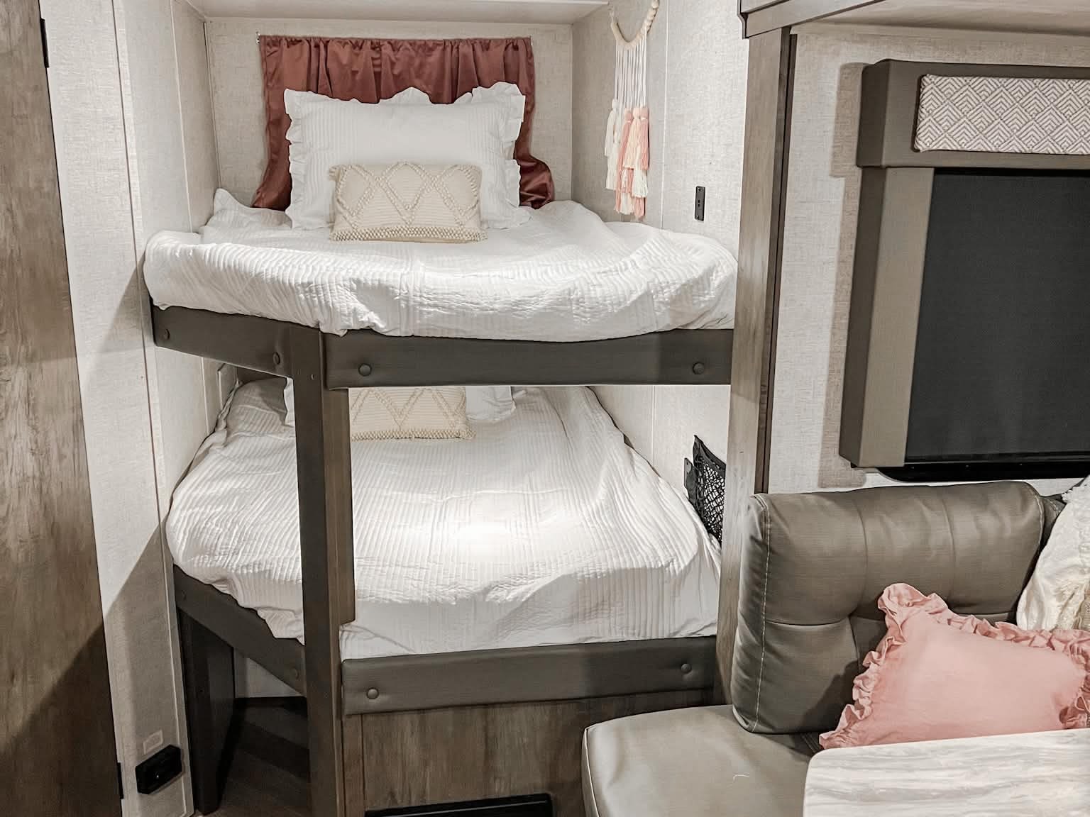 Cozy bunk beds with soft white bedding and stylish accents create an inviting RV rental interior, ideal for family adventures.. Forest River Wildwood X-Lite 2020
