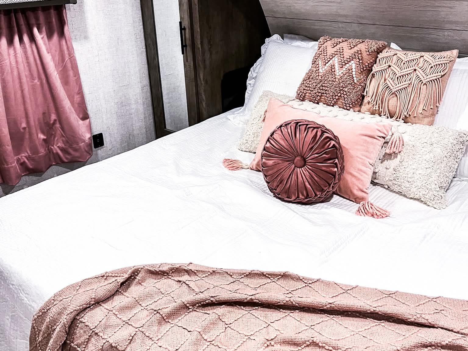 Cozy pink bedroom in an RV rental, featuring decorative pillows & a comfy throw. Perfect for glamping adventures.. Forest River Wildwood X-Lite 2020