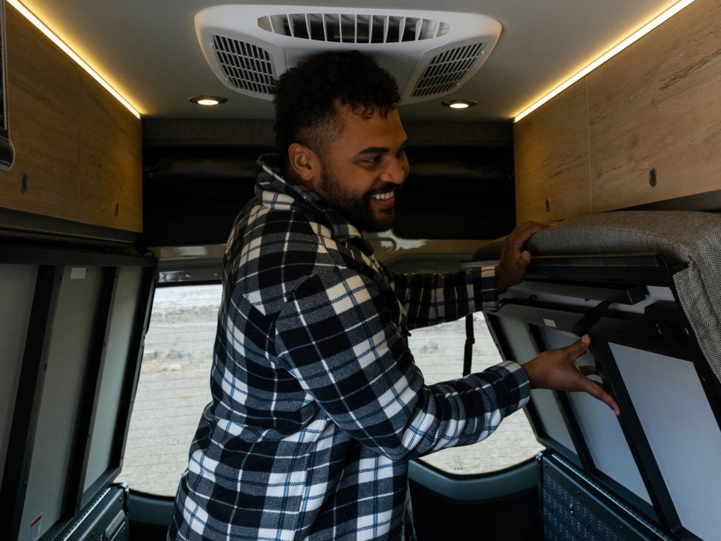 Smiling man adjusts a foldable bed inside his RV rental, ready for adventure and comfortable travel.. Storyteller Overland Beast MODE 4x4 2023