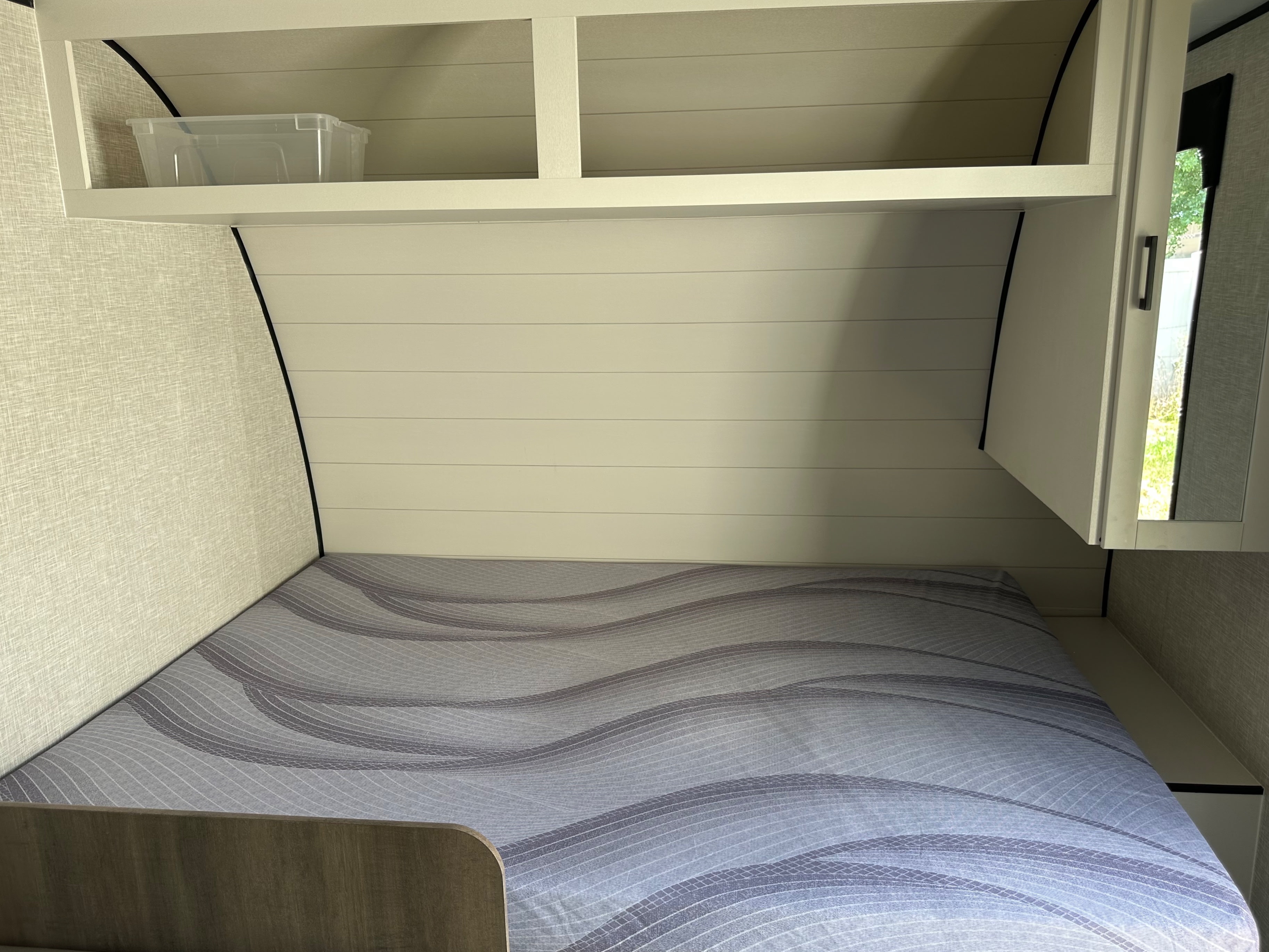 View of an RV rental bedroom with a grey wavy mattress, overhead storage cubbies, and a side cabinet revealing a window.. Highland Ridge RV Open Range Colt Edition 2026