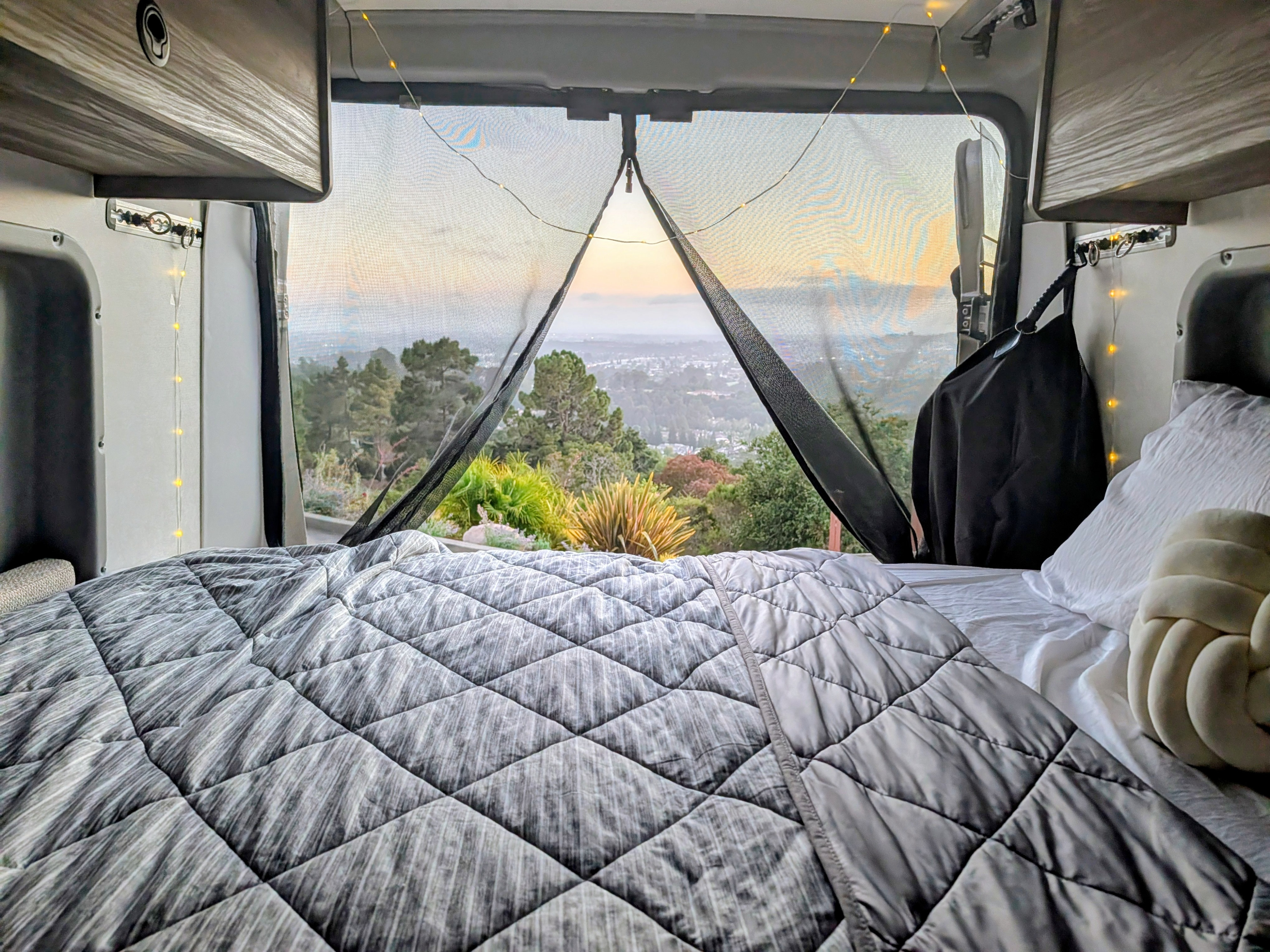 Inside a cozy RV rental: a plush bed, fairy lights, and panoramic nature views through a mesh screen. Perfect for van life.. Winnebago Solis 2025