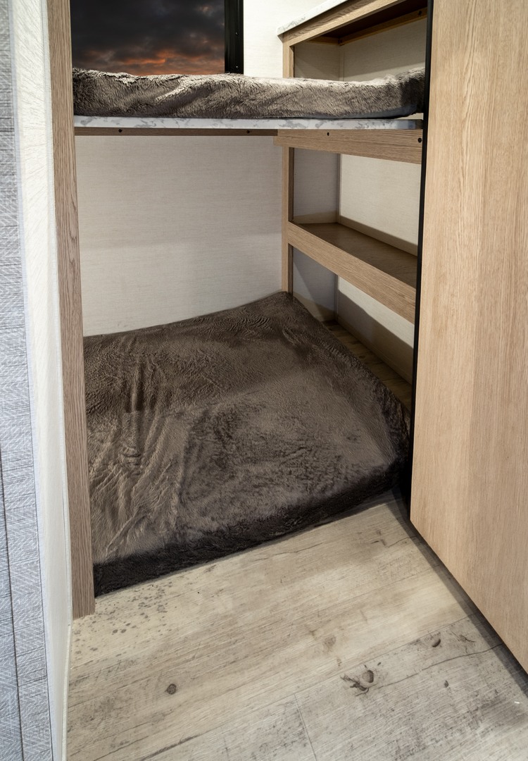RV rental interior shows bunk beds with dark plush bedding, light wood floor, and integrated shelves. Great for extra sleep.. Gulf Stream Amerilite 2026