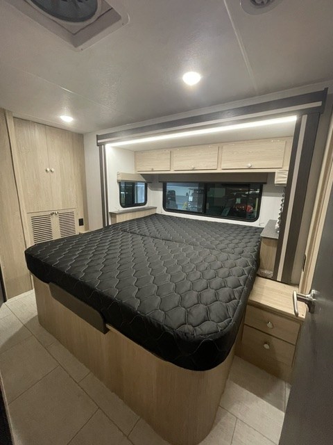This RV rental bedroom features a large, black quilted bed, light wood cabinets, and windows for natural light. A comfortable space.. Coachmen LEPERCHAUN 308KB 2027
