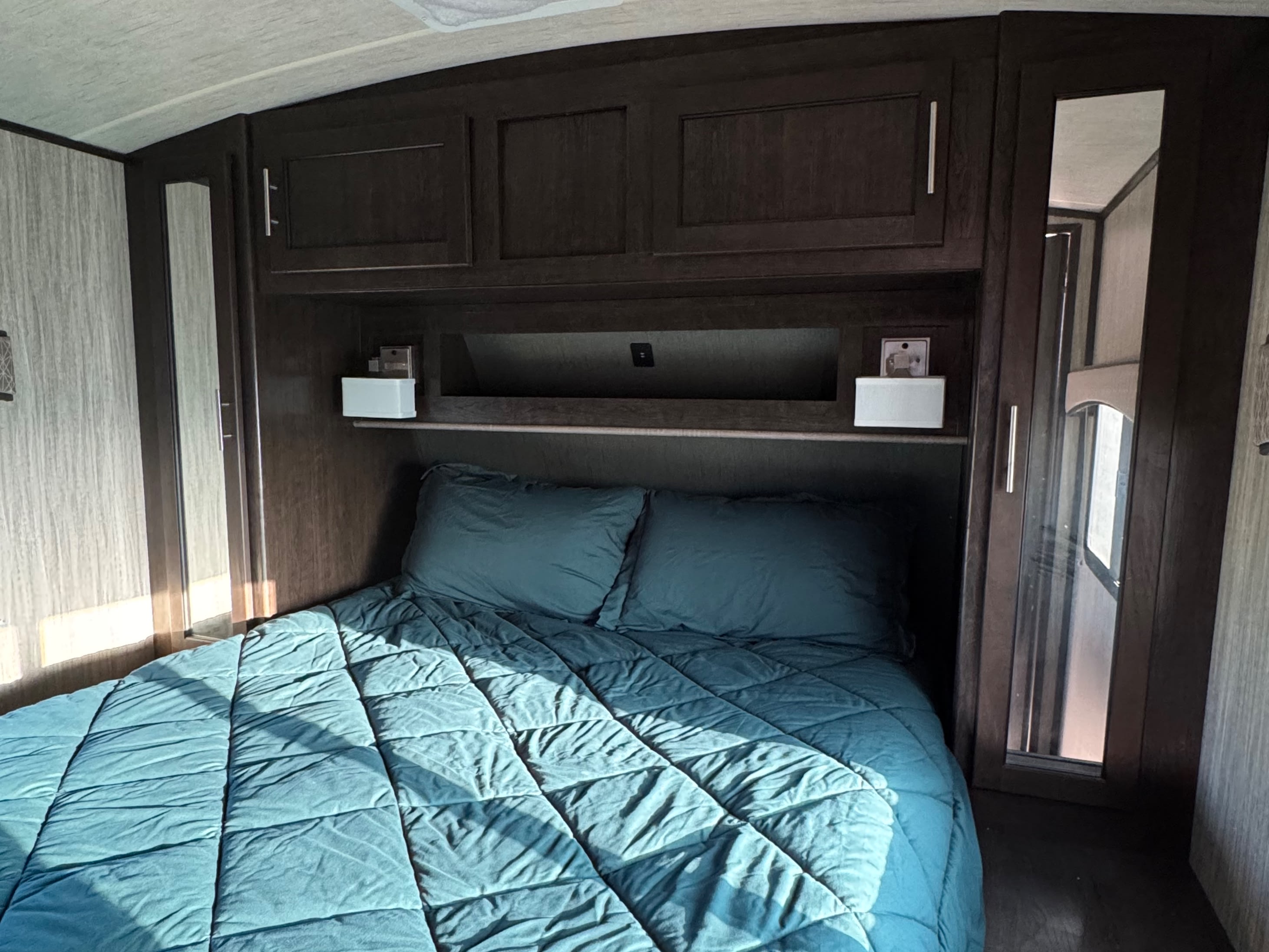 Comfortable RV rental bedroom with a teal bed, overhead cabinets, and mirrored closets, perfect for your next trip.. Cruiser RV Fun Finder Xtreme Lite 2019