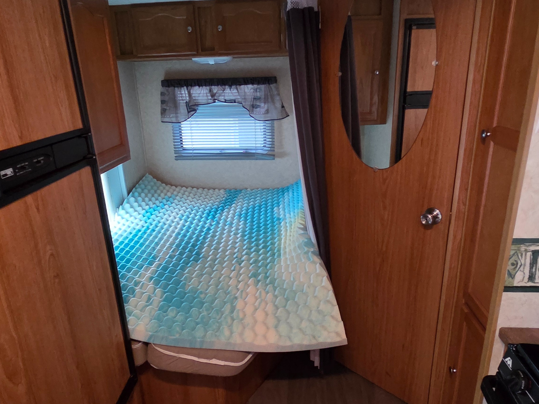 rv rental: A cozy camper bedroom with a bed featuring a blue-and-white wavy topper, window, wooden cabinets, and a fridge.. R-Vision Trail-Lite Trail-Cruiser 2007