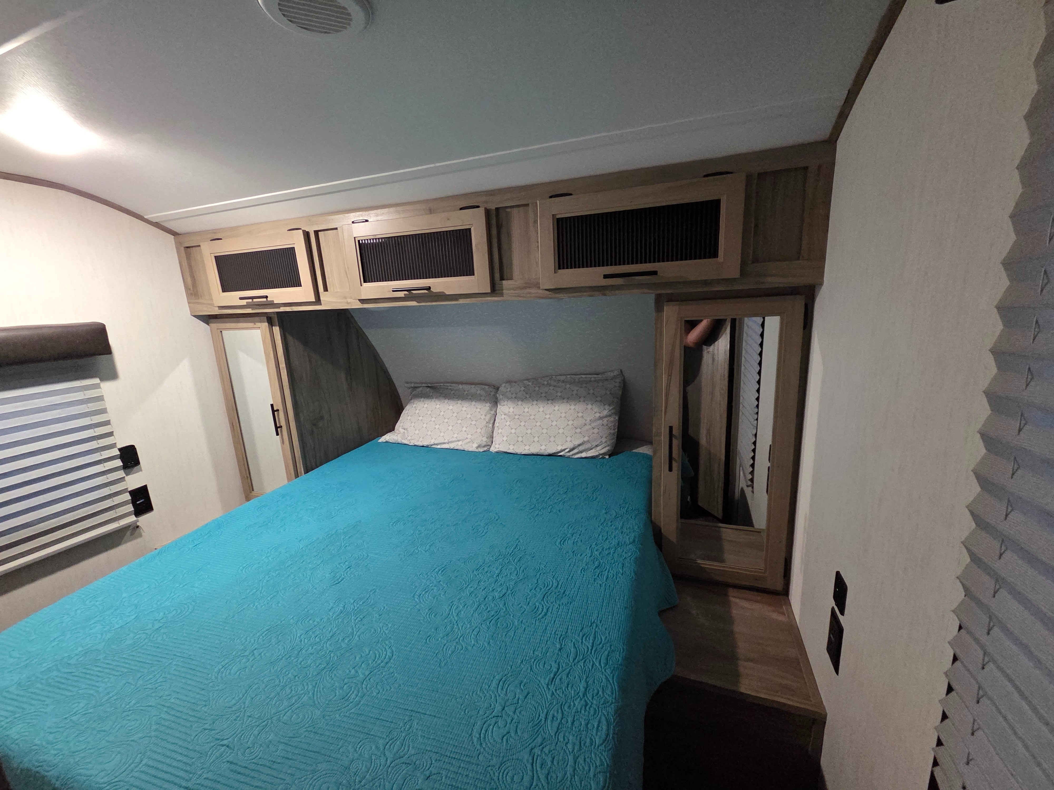 Cozy RV rental bedroom featuring a blue bedspread, overhead storage, and mirrored closets for a comfortable stay.. Forest River Cherokee Alpha Wolf 2022