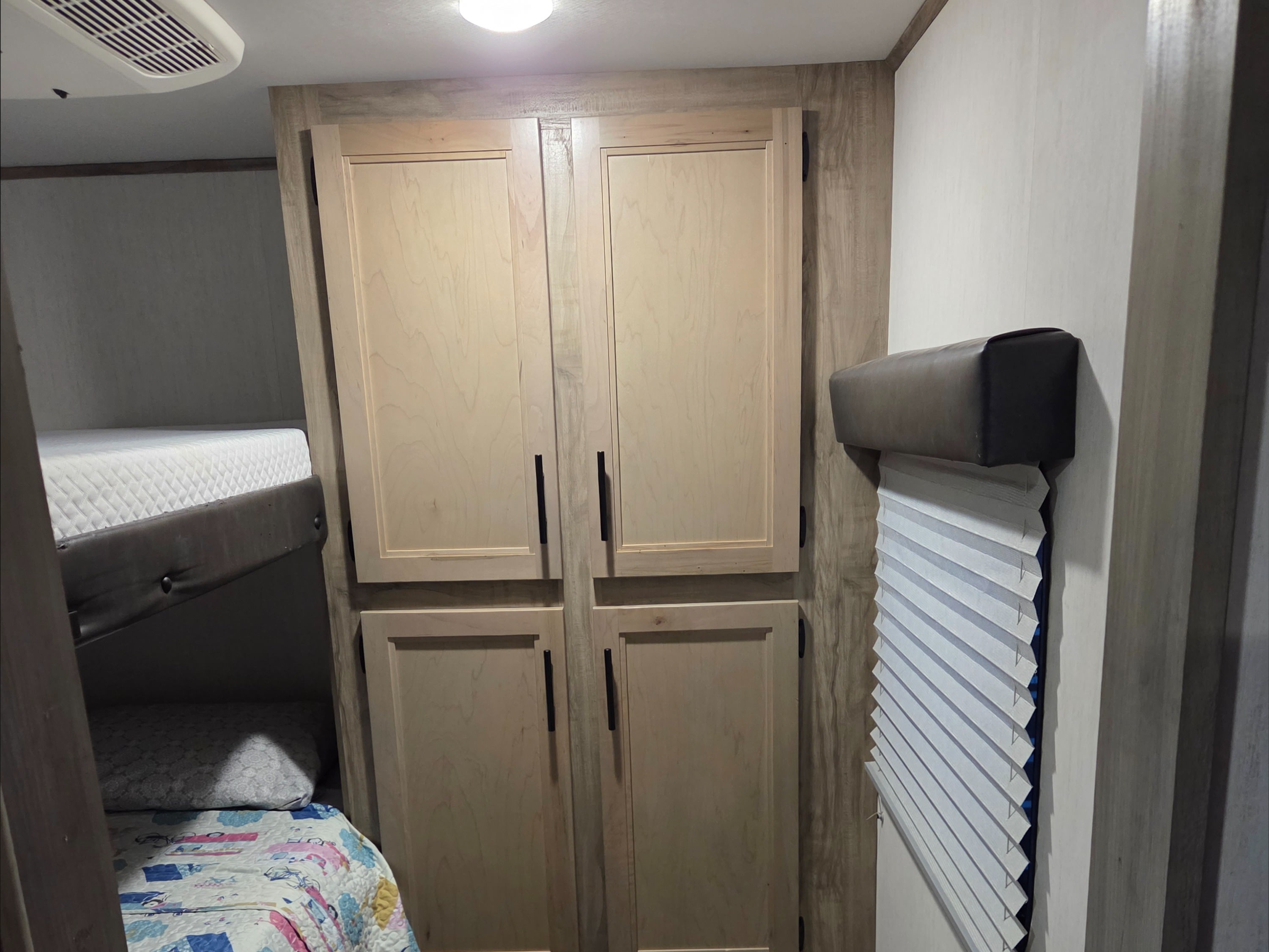 RV rental interior: bunk beds with bedding, light wood storage cabinets, and a window with blinds. Functional and compact.. Forest River Cherokee Alpha Wolf 2022
