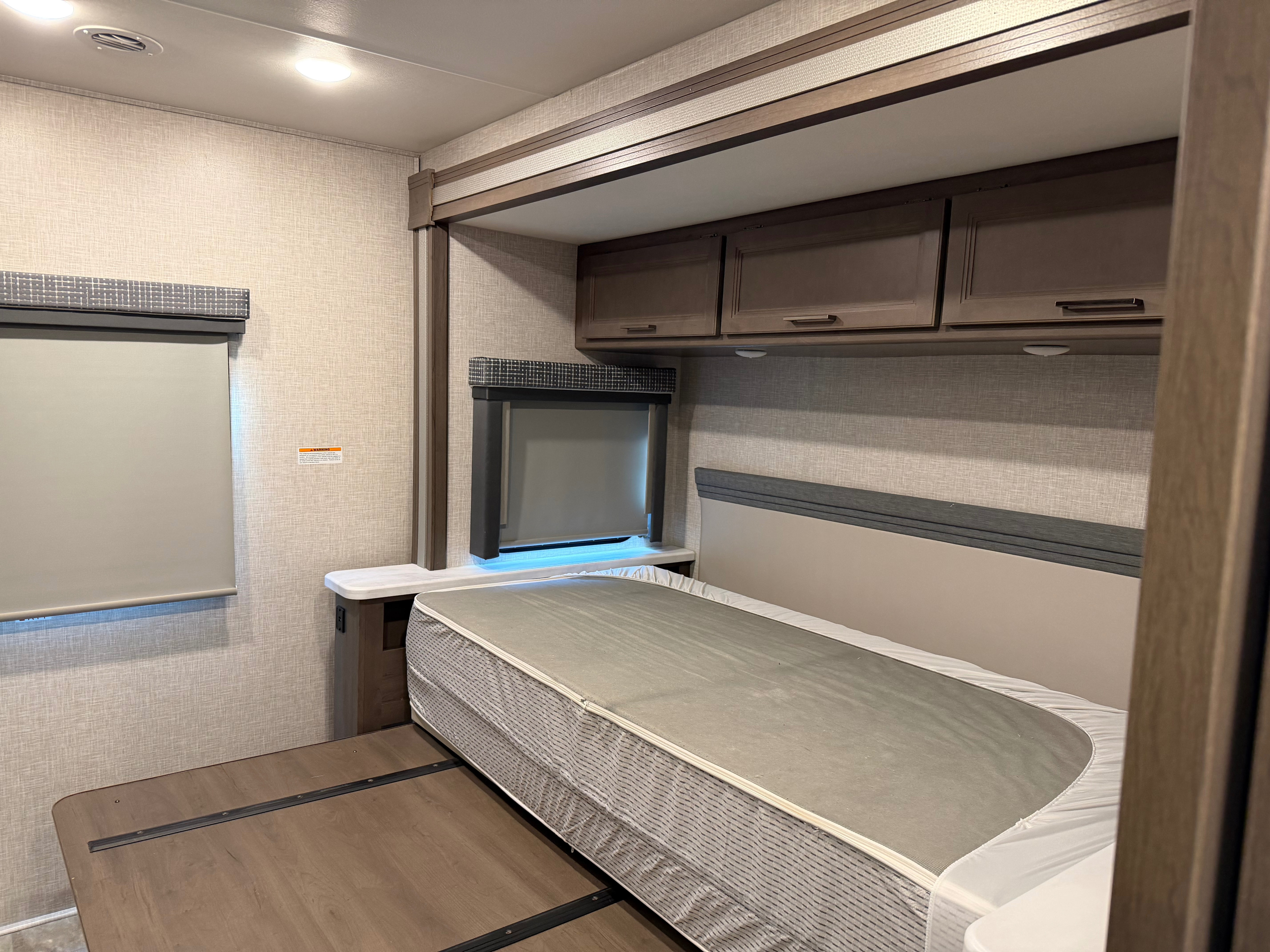 RV rental bedroom: Interior view showing a bed, overhead storage cabinets, and two windows with blinds.. Thor Windsport 2023