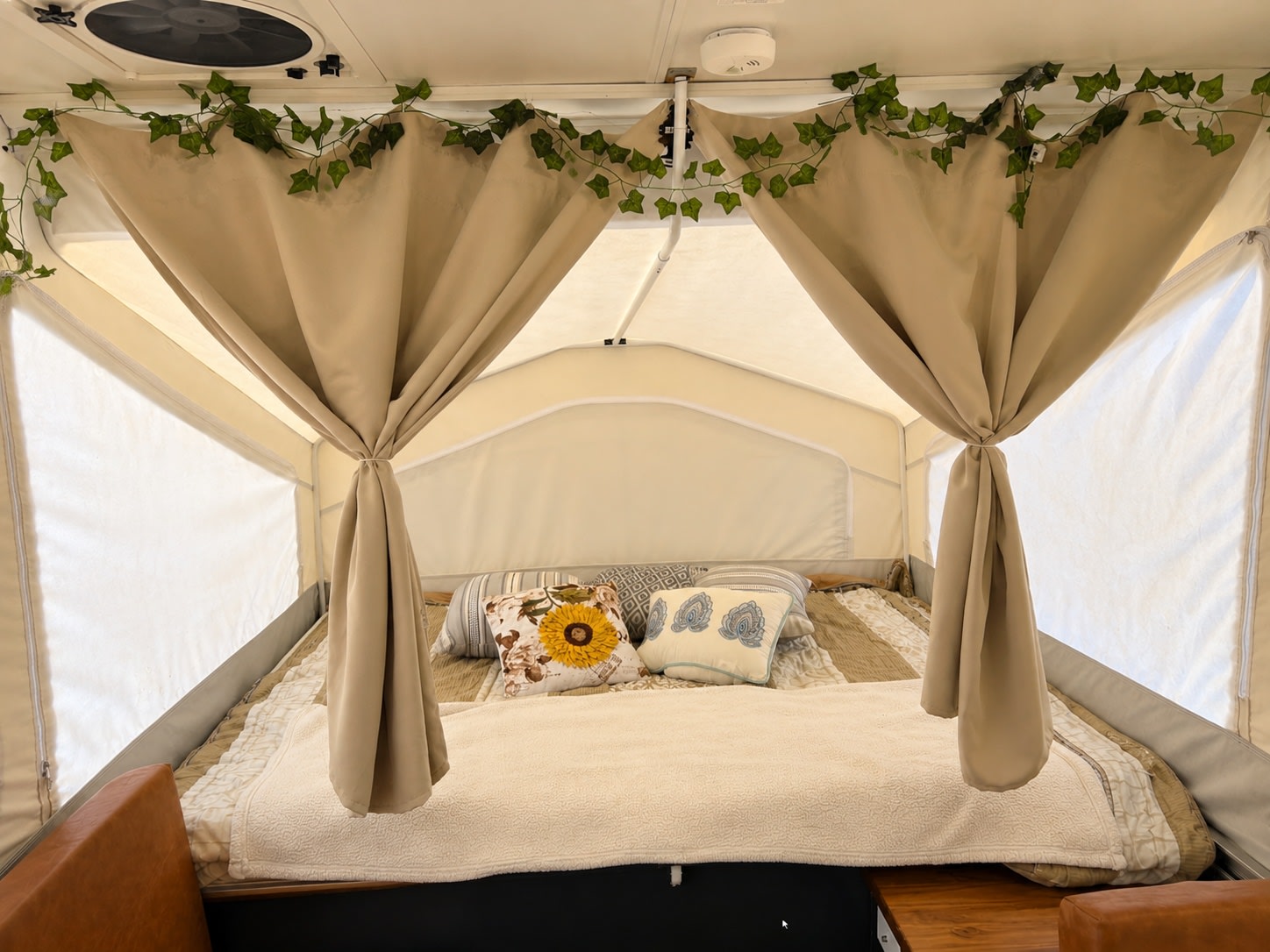 Inside a decorated RV rental pop-up camper bedroom featuring a comfy bed, draped curtains, and charming ivy garland.. Rockwood Freedom 231 2014